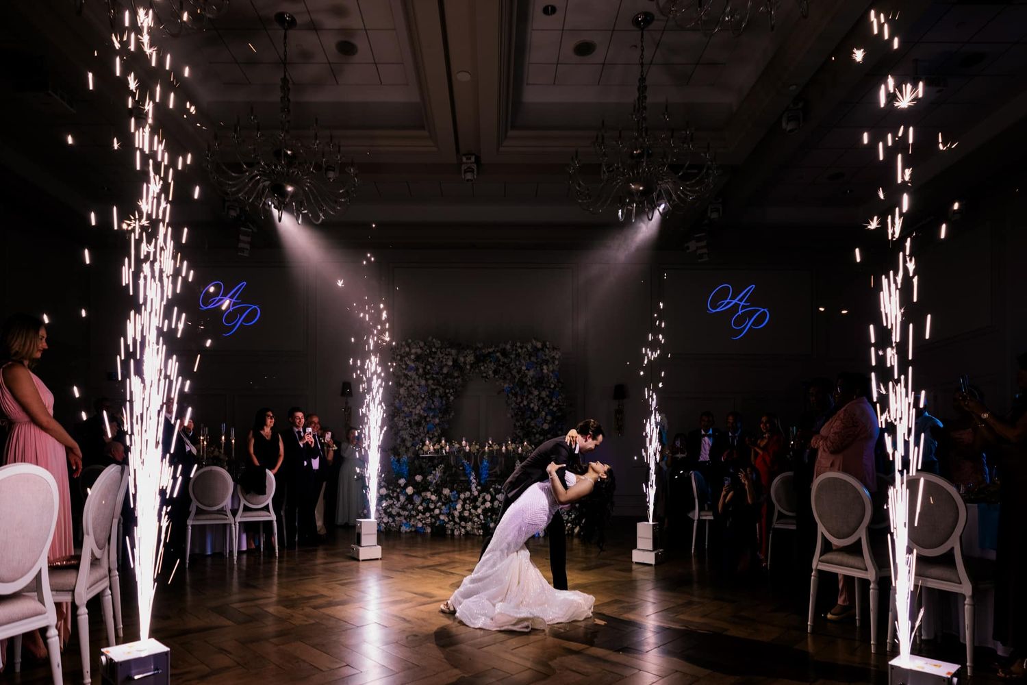 Bride and groom share first dance kiss surrounded by sparkling cold firework fountains in darkened reception hall.
