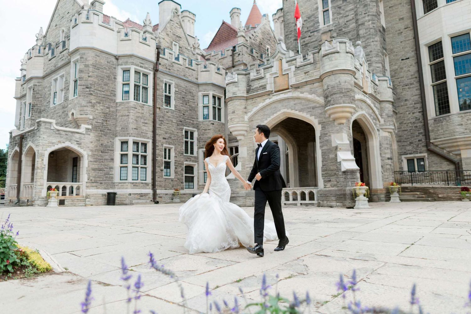Elegant bride and groom walk hand in hand across a stone courtyard of a historic castle venue.