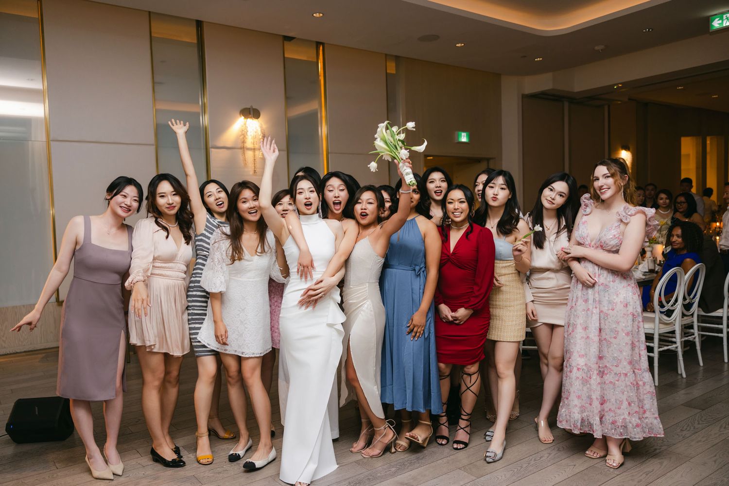 Bride in white gown poses with a large group of female friends after the bouquet toss at reception.