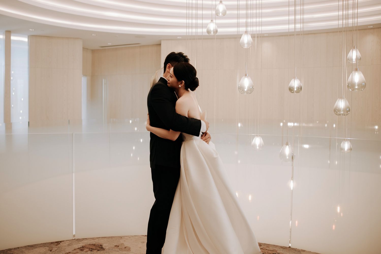 Bride and groom share romantic embrace in elegant white wedding venue.