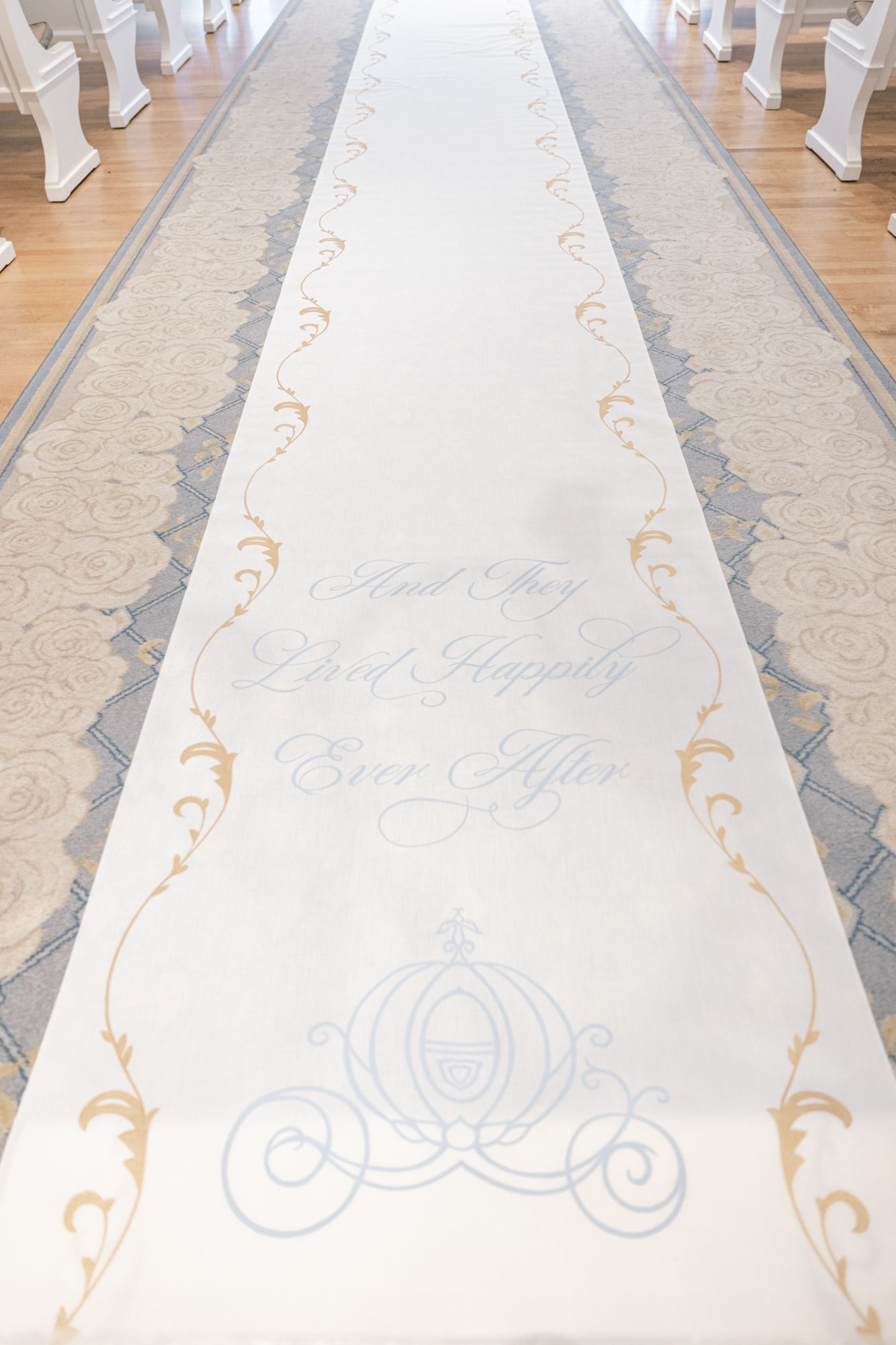 White wedding aisle runner with gold floral designs and Cinderella carriage reading And They Lived Happily Ever After.