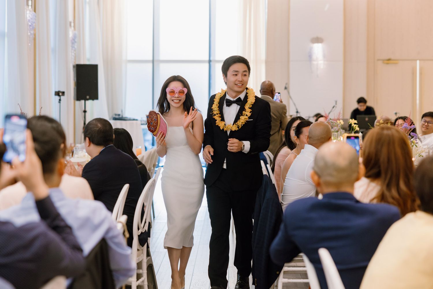 Couple making grand entrance at wedding reception as guests celebrate and take photos.