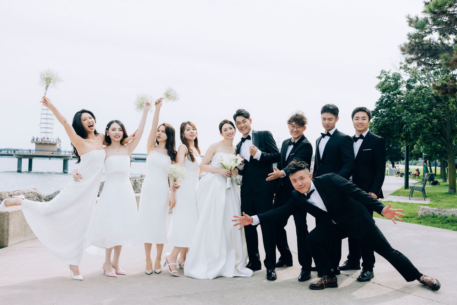 Wedding party in black and white attire pose playfully by the waterfront.