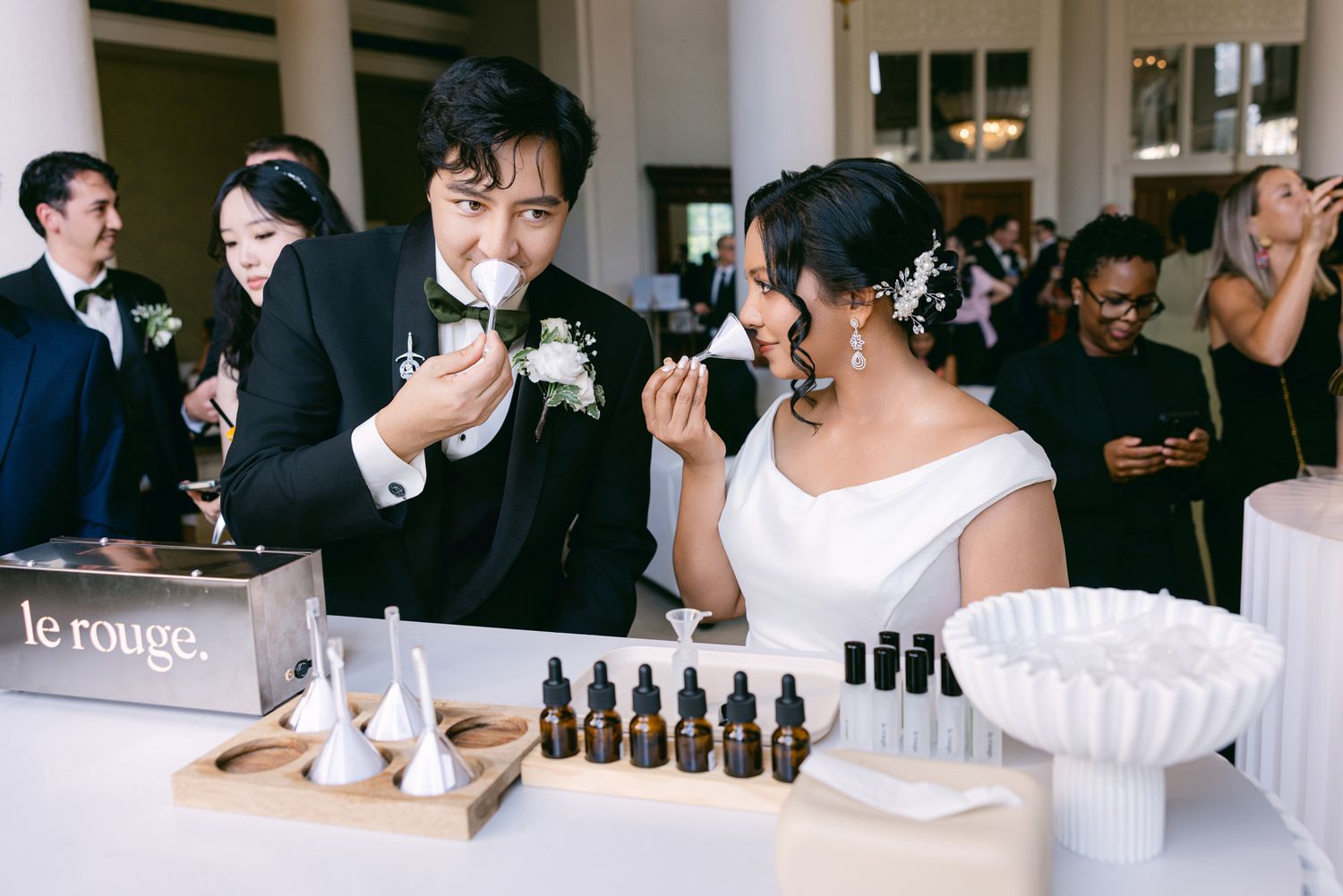 Bride and groom smell scented perfume blotters at a custom fragrance bar with oil bottles during their wedding reception.
