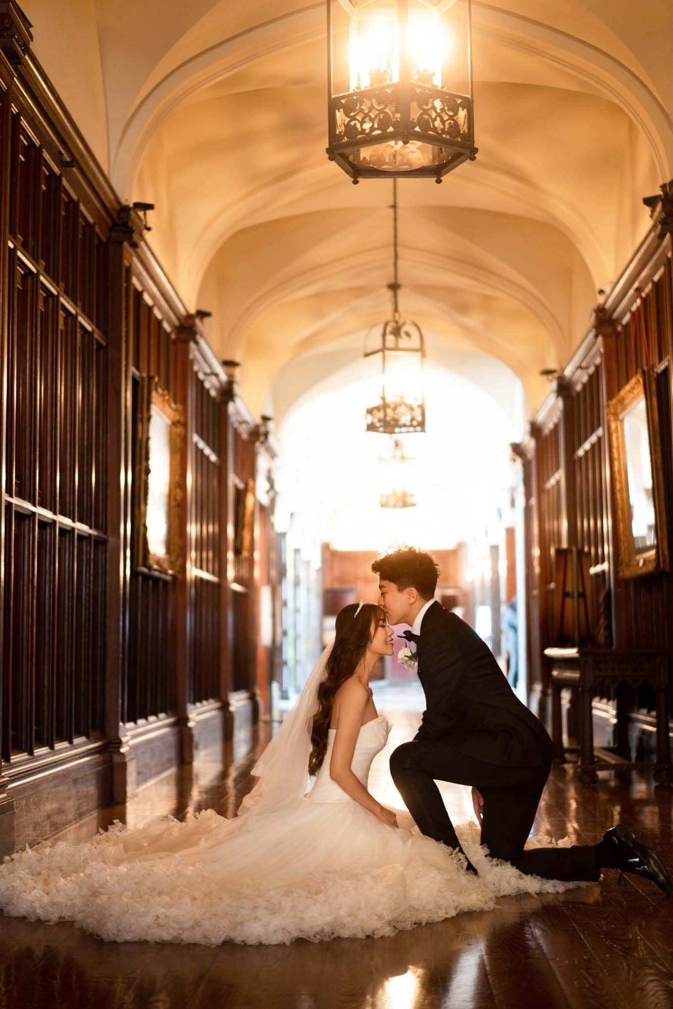 Bride and groom share a kiss in an elegant vaulted hallway with ornate chandeliers.
