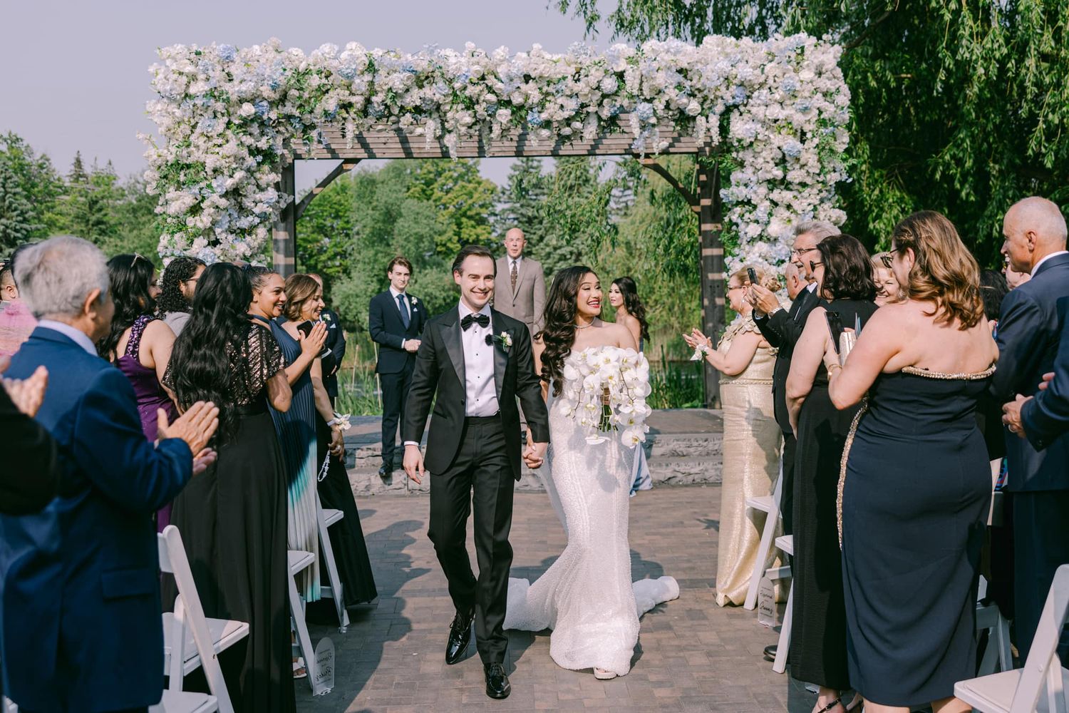 Joyful newlyweds walk back down aisle as guests celebrate under floral arch.