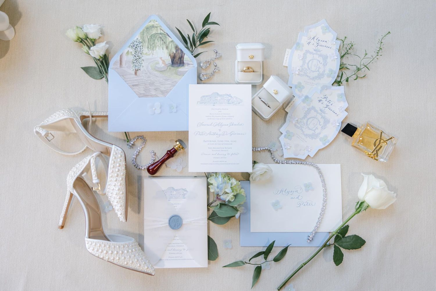 Elegant blue and white wedding invitation suite with wax seal, white heels, and florals.