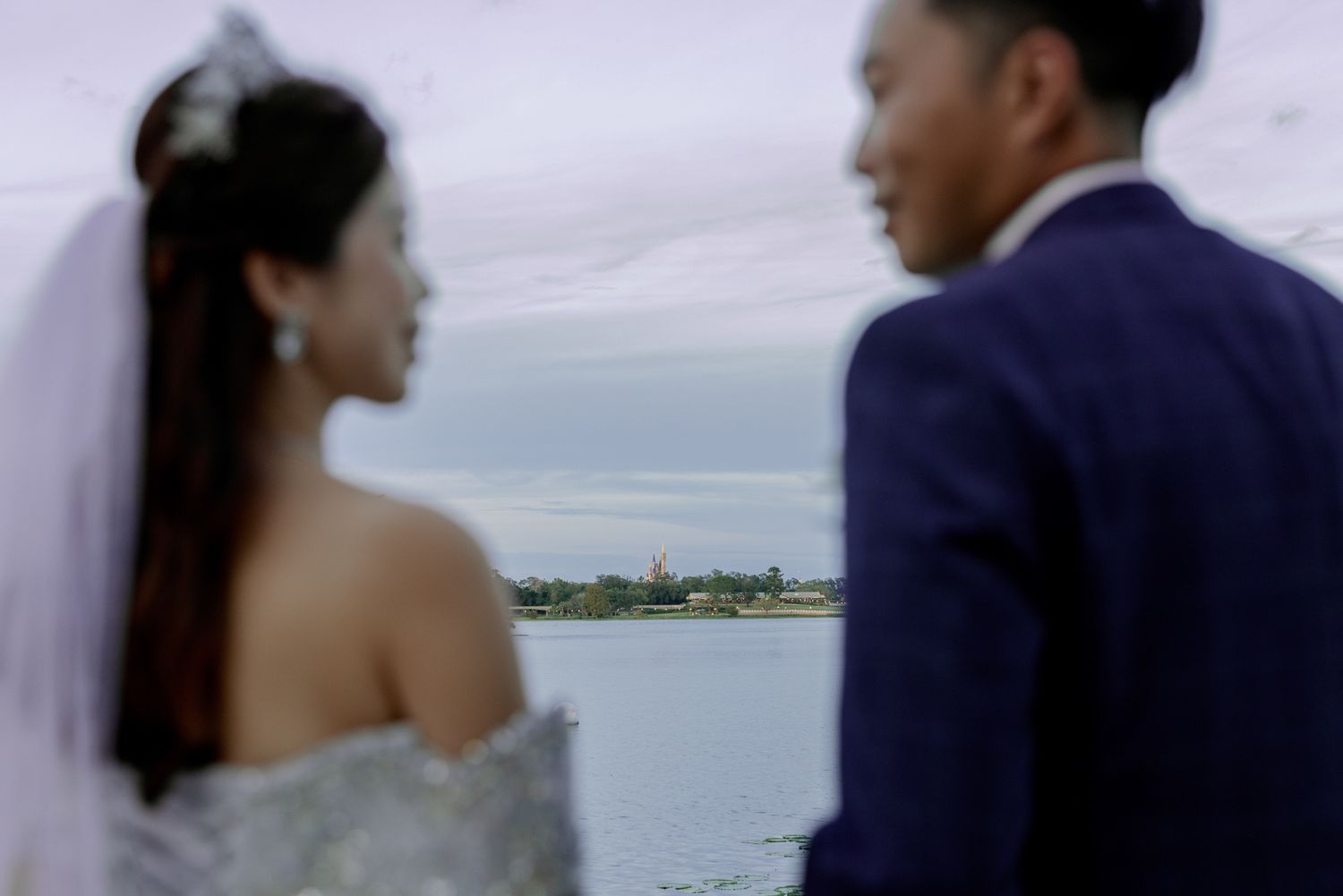 Bride and groom in wedding attire share a romantic moment overlooking a serene waterfront at dusk.