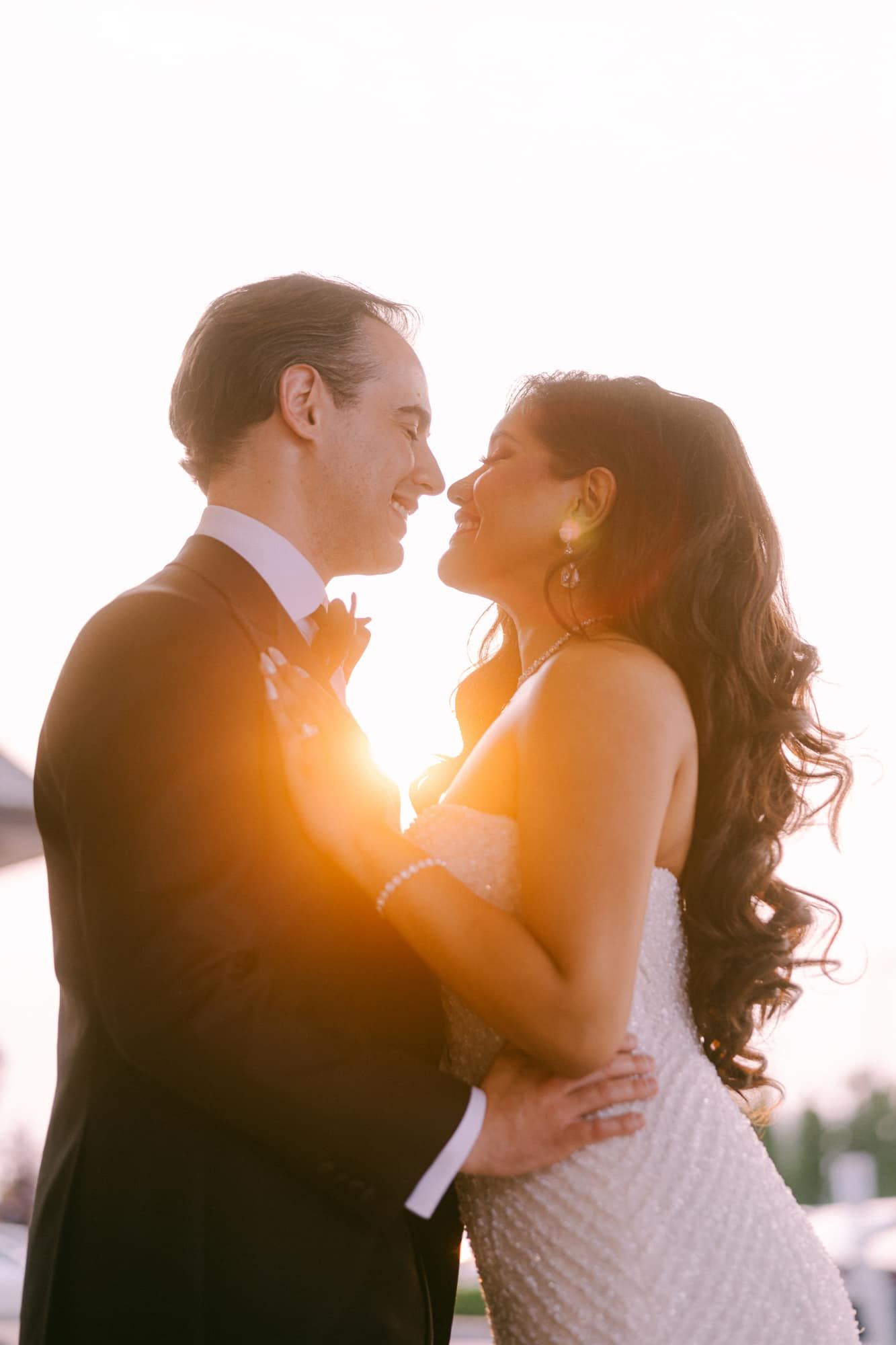 Bride and groom share a romantic moment silhouetted against a glowing golden sunset light.