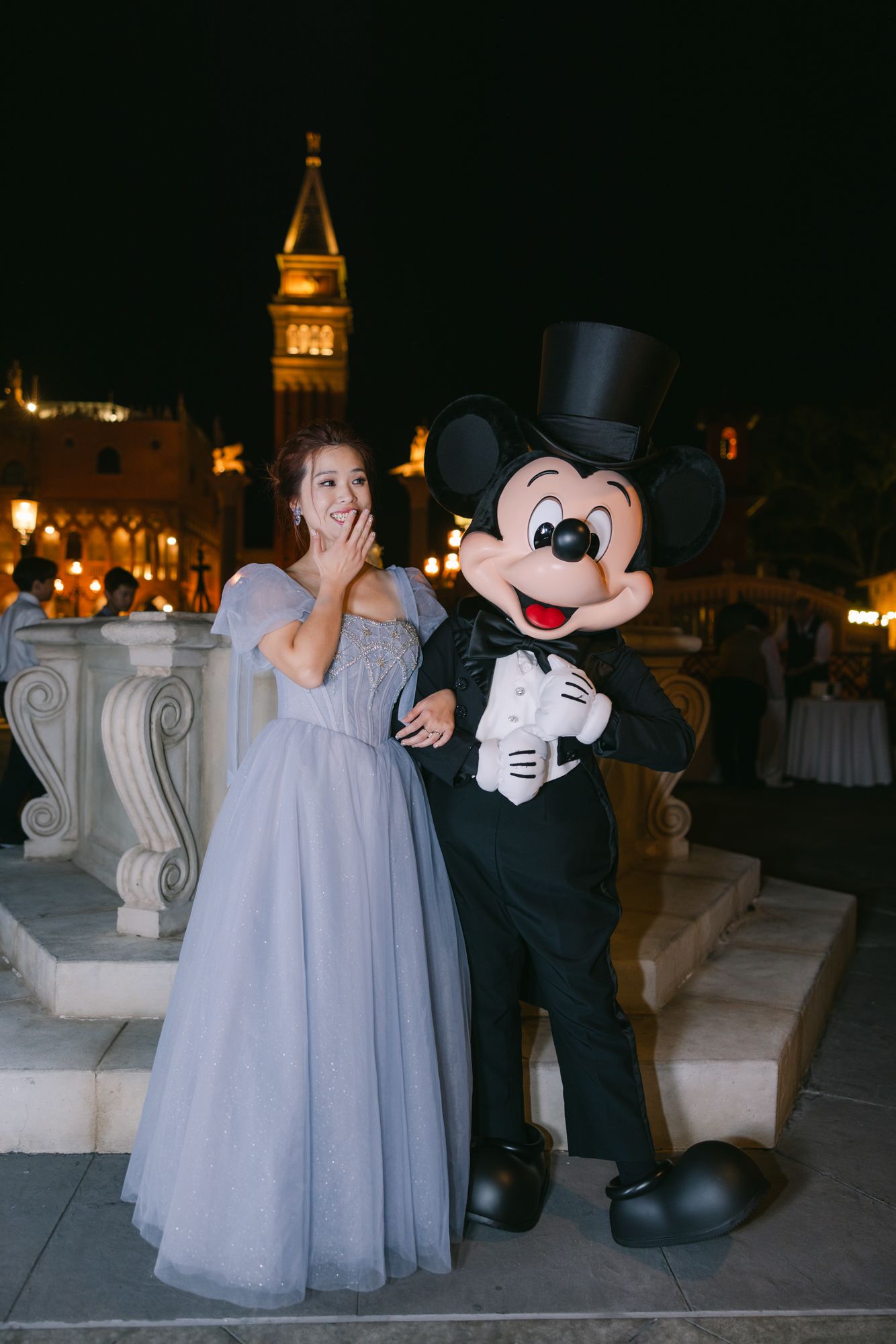 Surprised bride in blue gown posing with Mickey Mouse in tuxedo at a Disney-themed wedding reception.