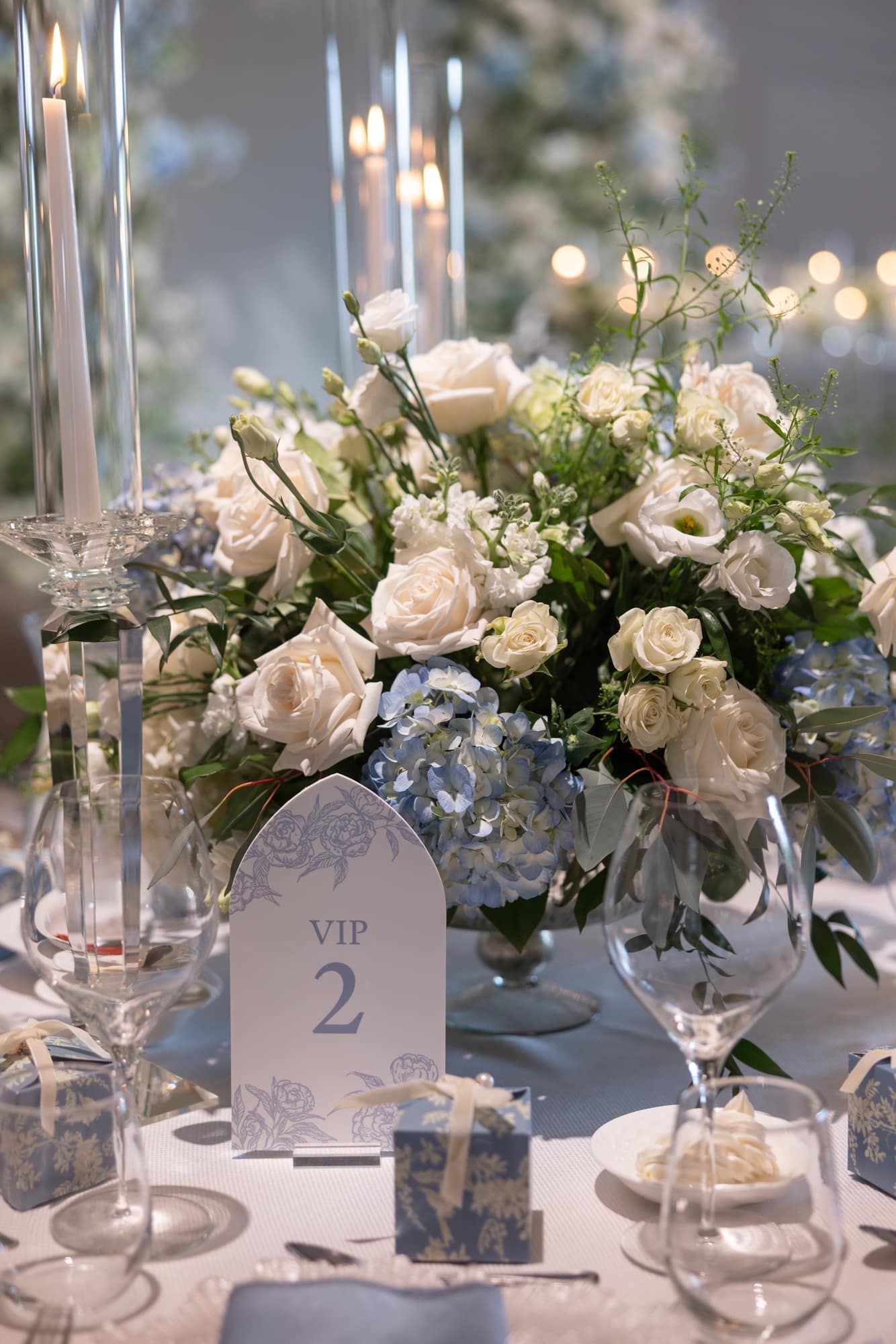 Elegant VIP wedding table setting with white roses, blue hydrangeas, crystal candles, and table number.