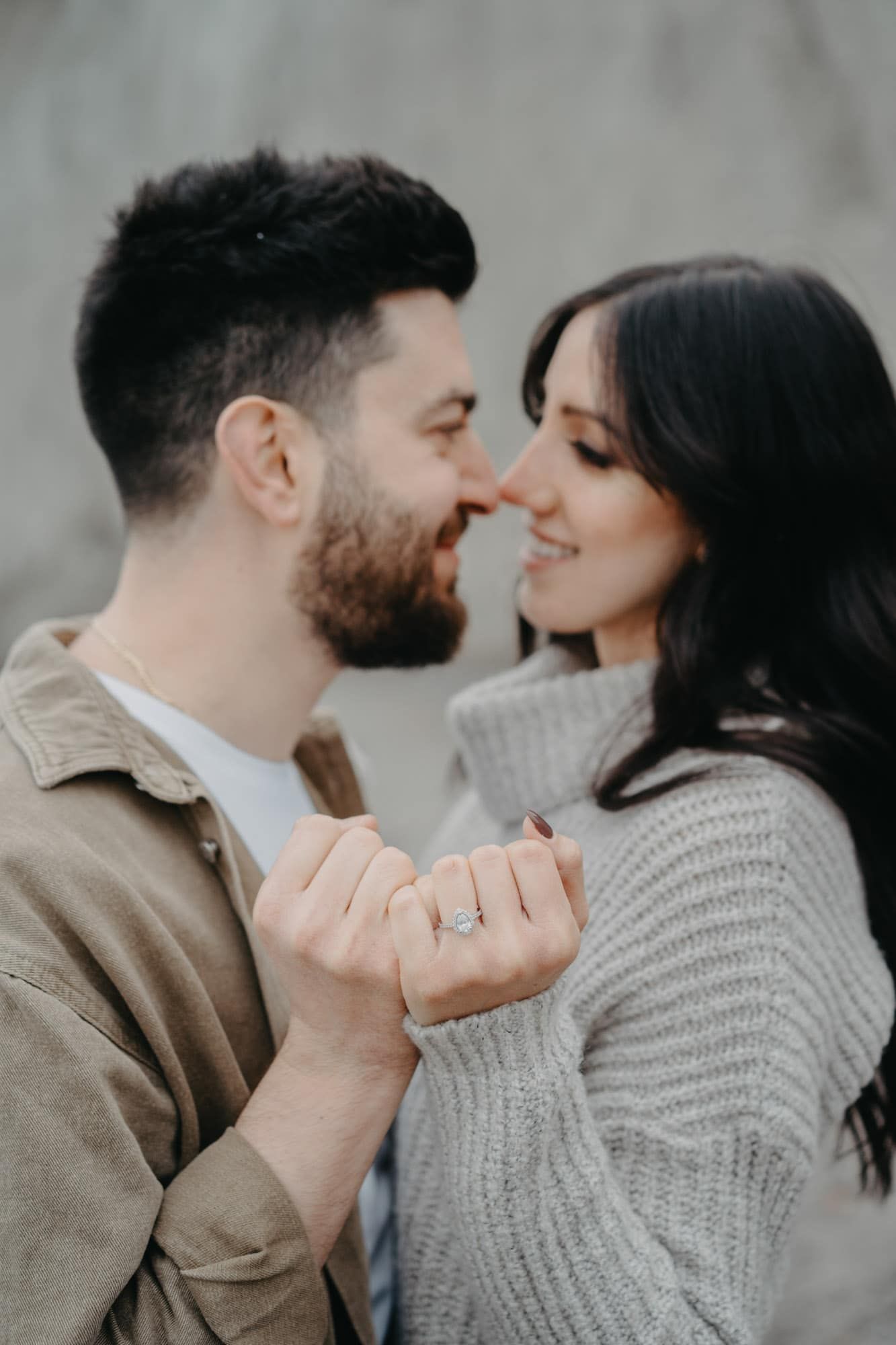 Close-up of smiling couple nearly kissing while holding hands showing engagement ring.
