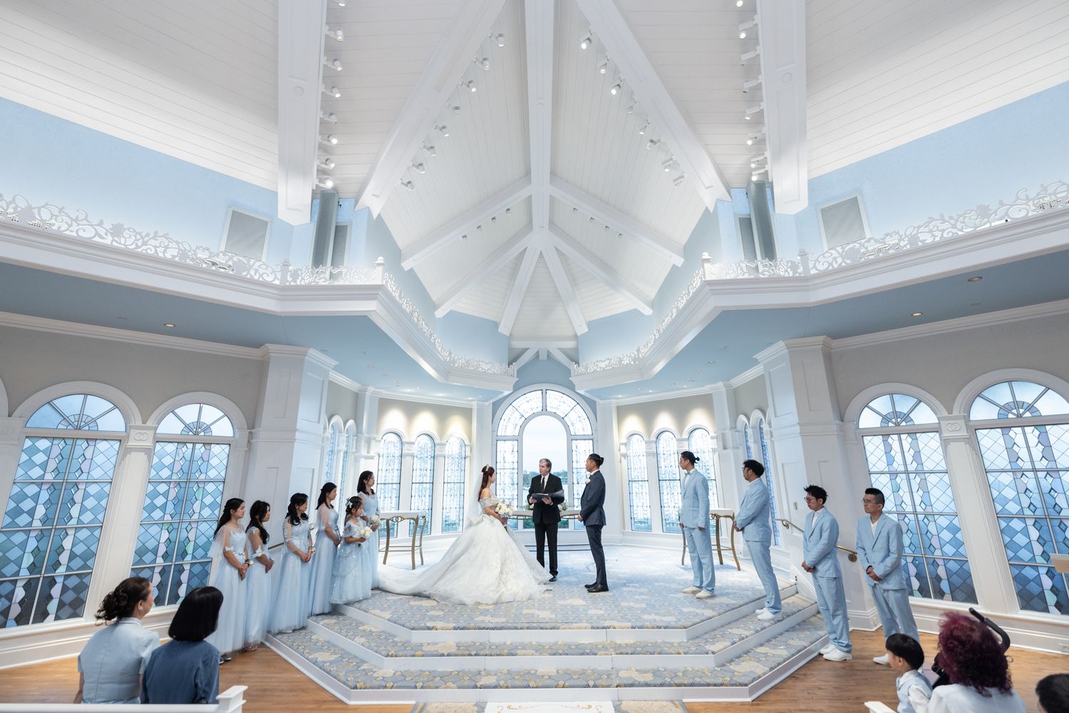 Wedding ceremony in stunning white chapel with bride, groom, and wedding party on grand staircase.