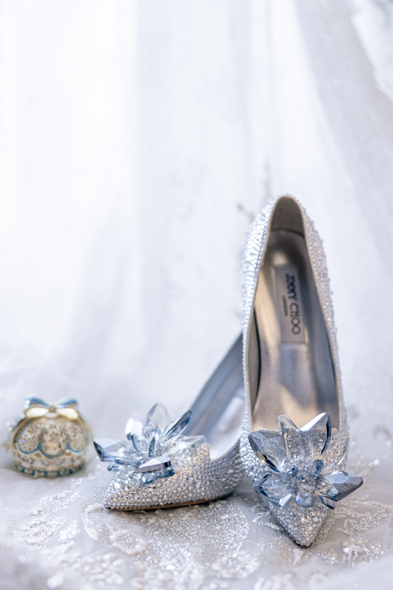 Crystal-embellished Jimmy Choo wedding heels with blue gem flowers on lace fabric with decorative accessories.