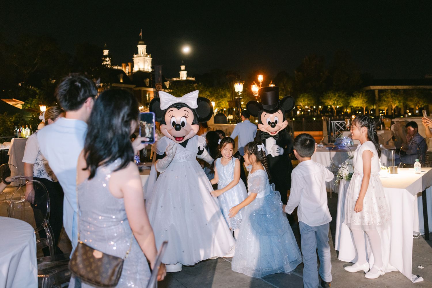 Mickey and Minnie Mouse characters mingle with wedding guests in blue attire at Disney park reception.