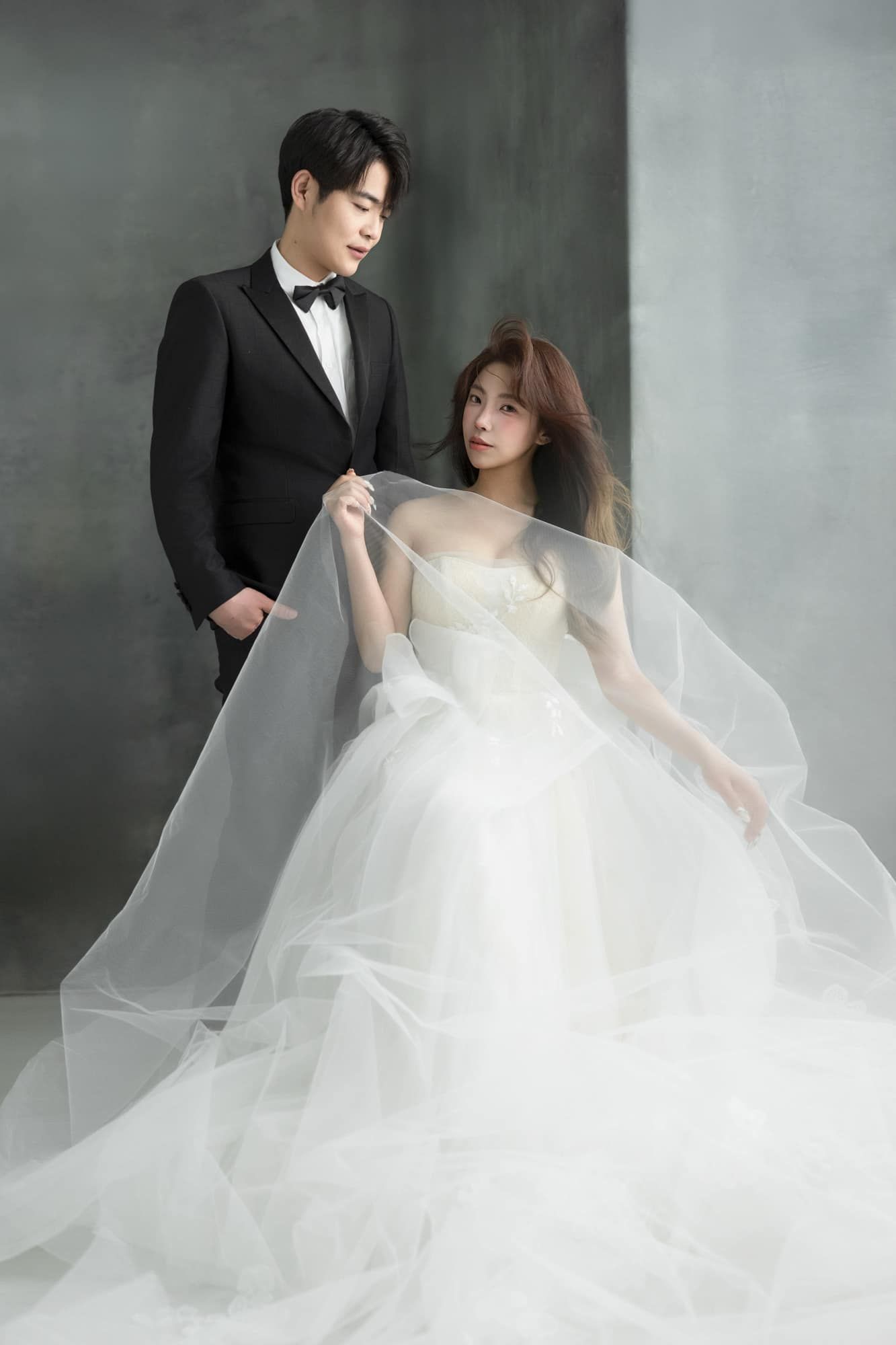 Elegant couple in wedding attire, man in black tuxedo and woman in flowing white ball gown, studio portrait.
