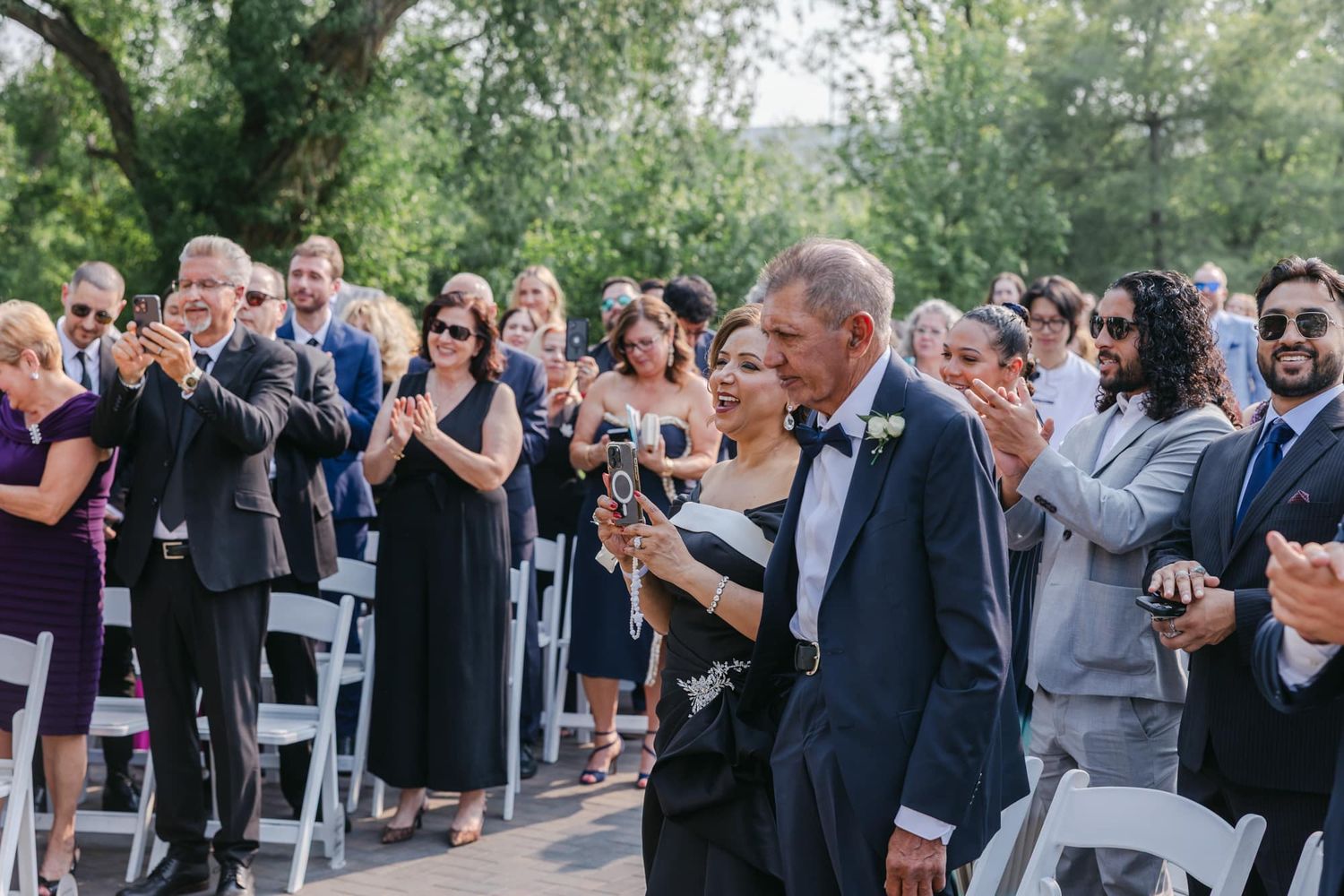 Wedding guests applaud as couple walks down outdoor aisle after ceremony.