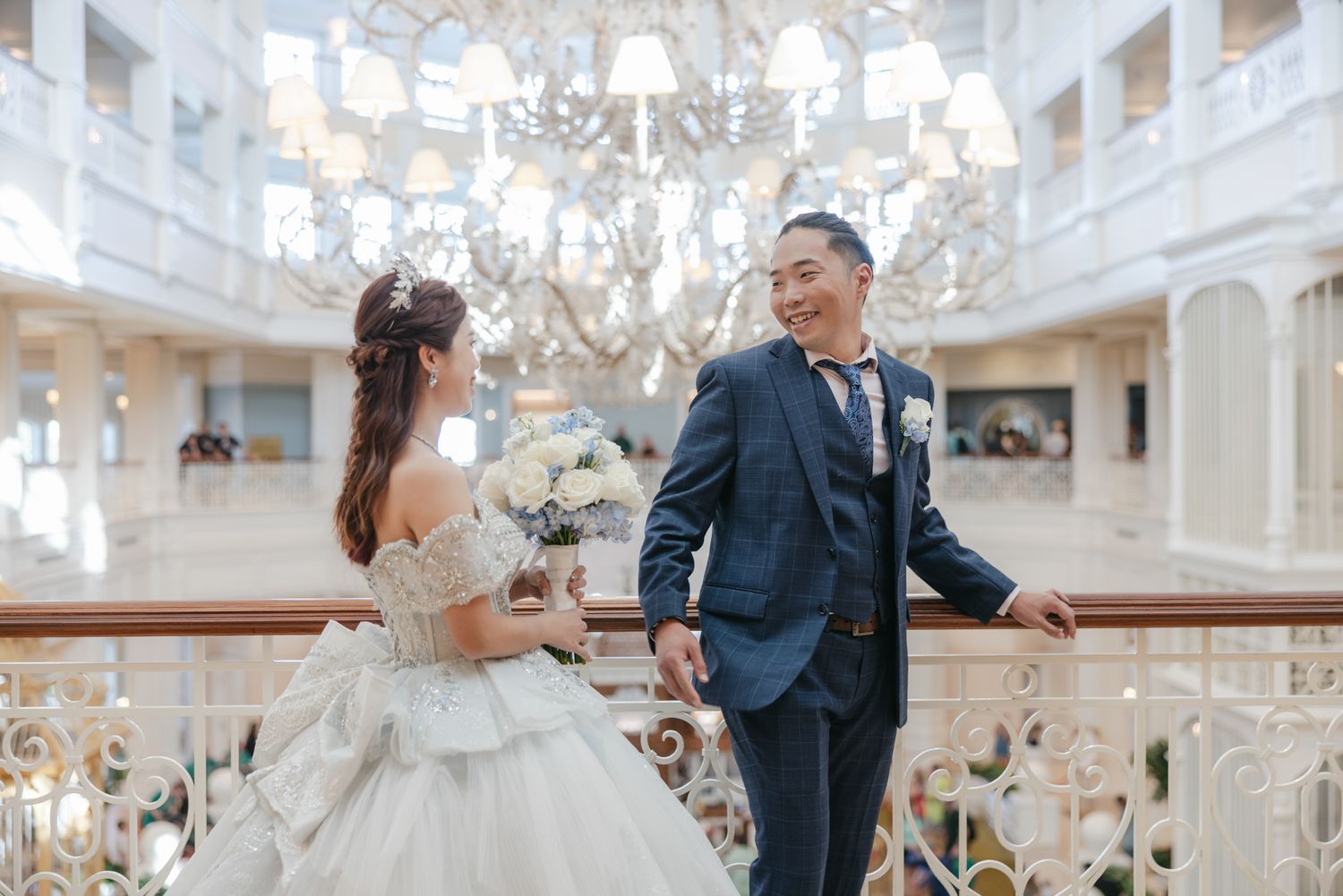 Bride and groom share romantic moment on grand staircase under crystal chandelier in elegant venue.