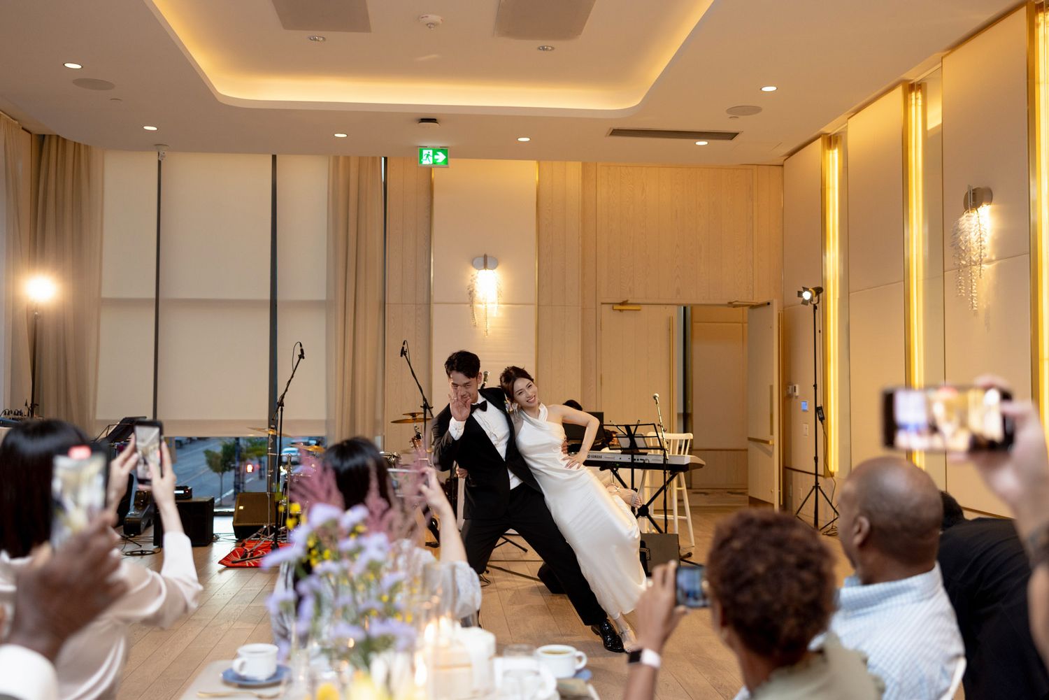 Bride and groom sharing first dance at wedding reception while guests capture moments on phones.
