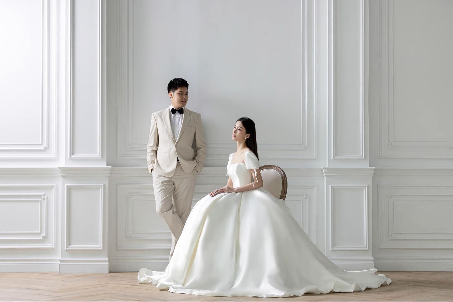 Korean-style wedding couple in minimalist white studio with bride seated in ball gown.