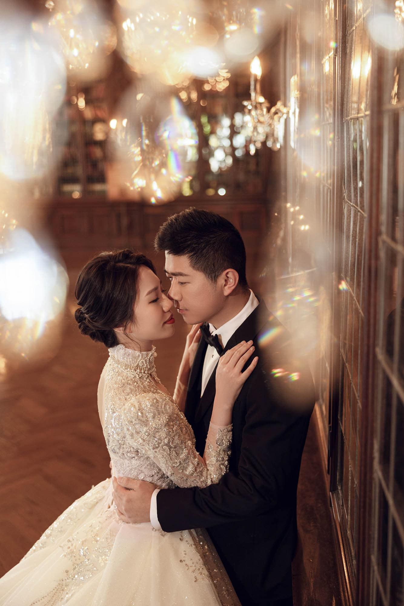 Romantic Asian couple in wedding attire sharing an intimate moment surrounded by warm bokeh lights.