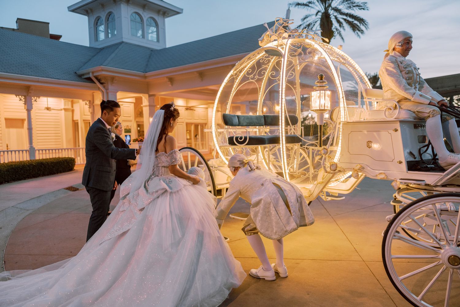 Bride and groom pose beside a glowing Cinderella carriage at a Disney wedding venue at dusk.
