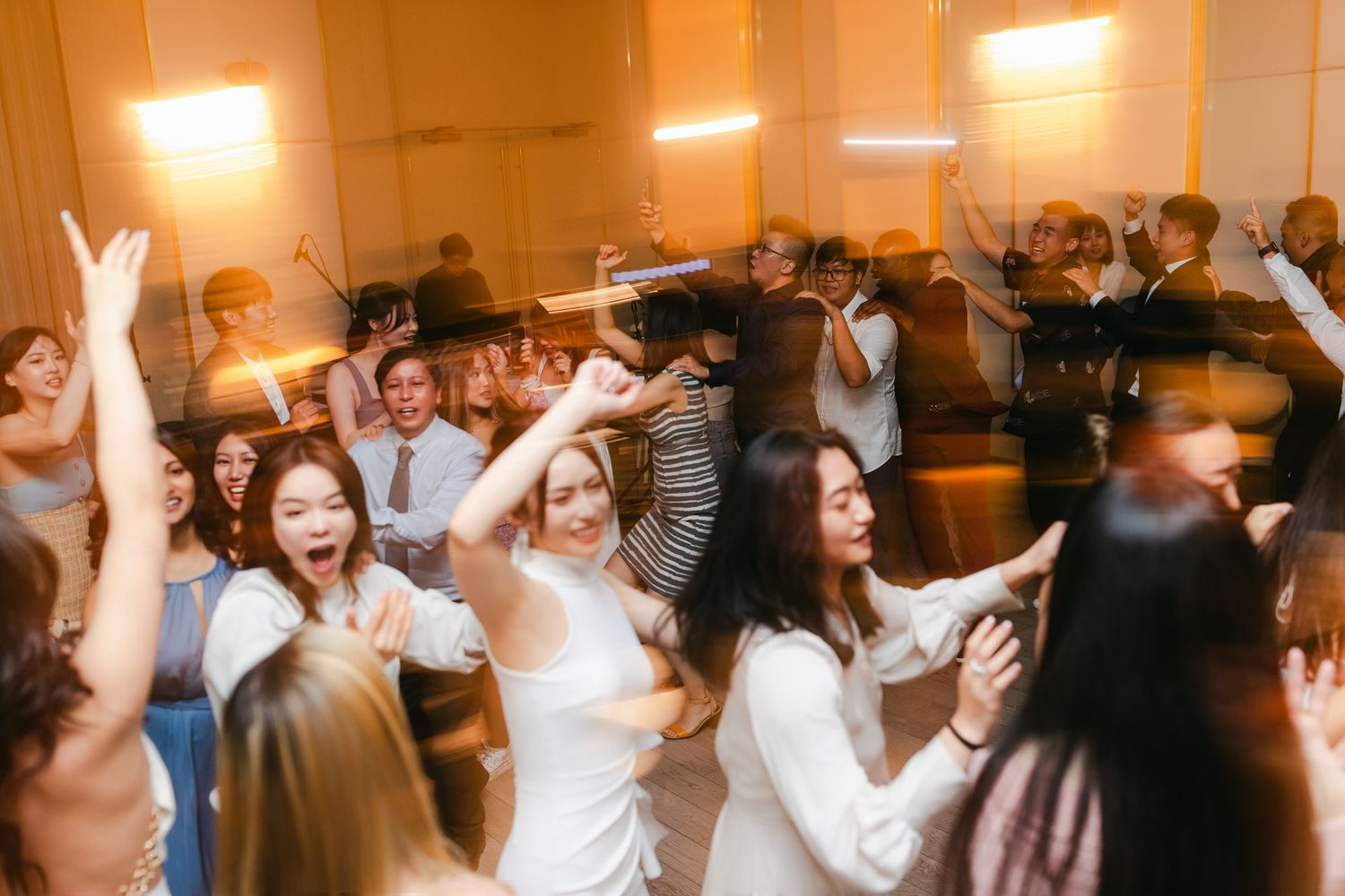 Guests dancing energetically at a wedding reception party in a warmly lit venue.