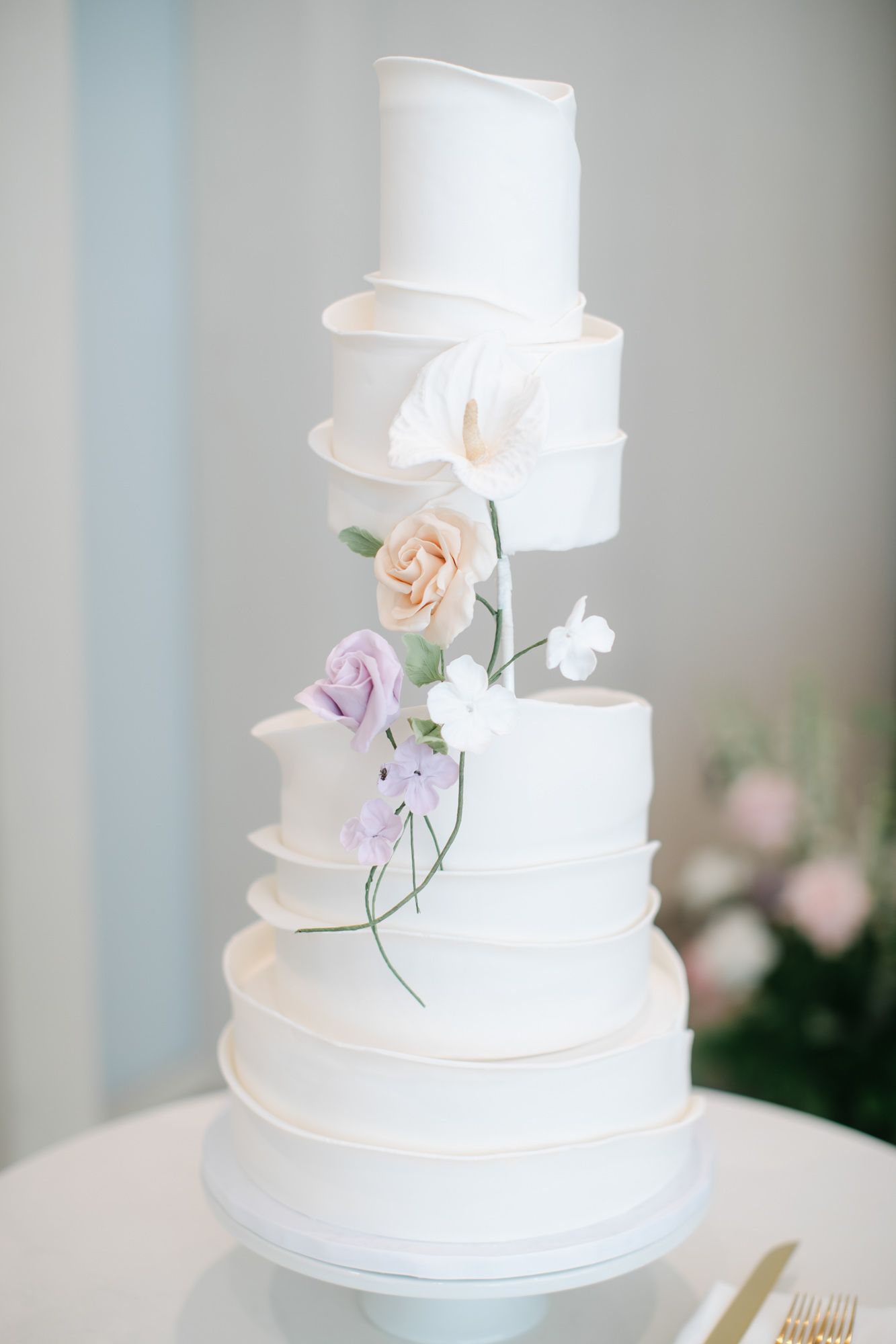 Four-tier white wedding cake adorned with delicate sugar flowers in pink and lavender hues.