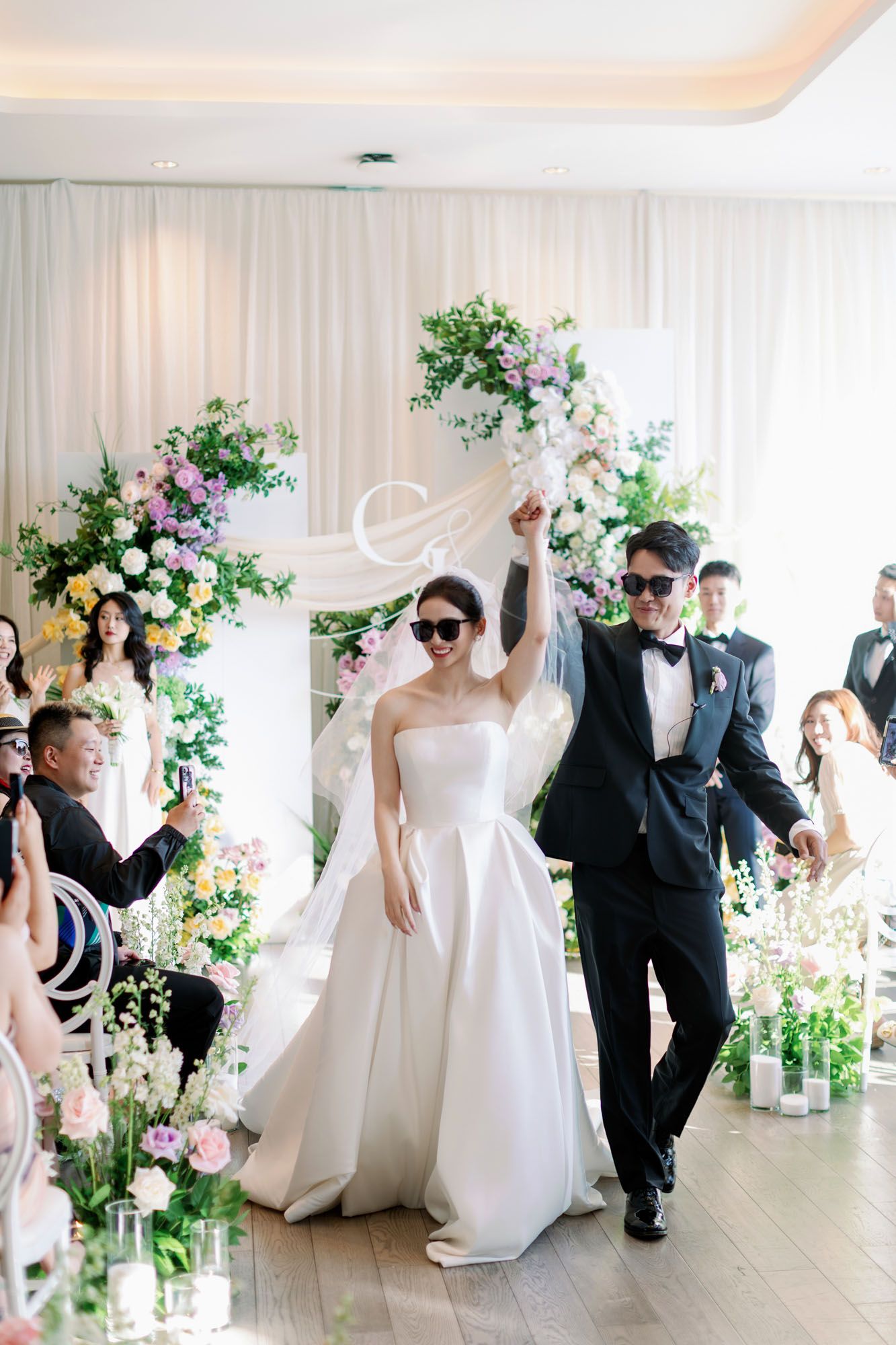 Newlyweds wearing sunglasses celebrate joyfully while walking back down aisle after wedding ceremony.