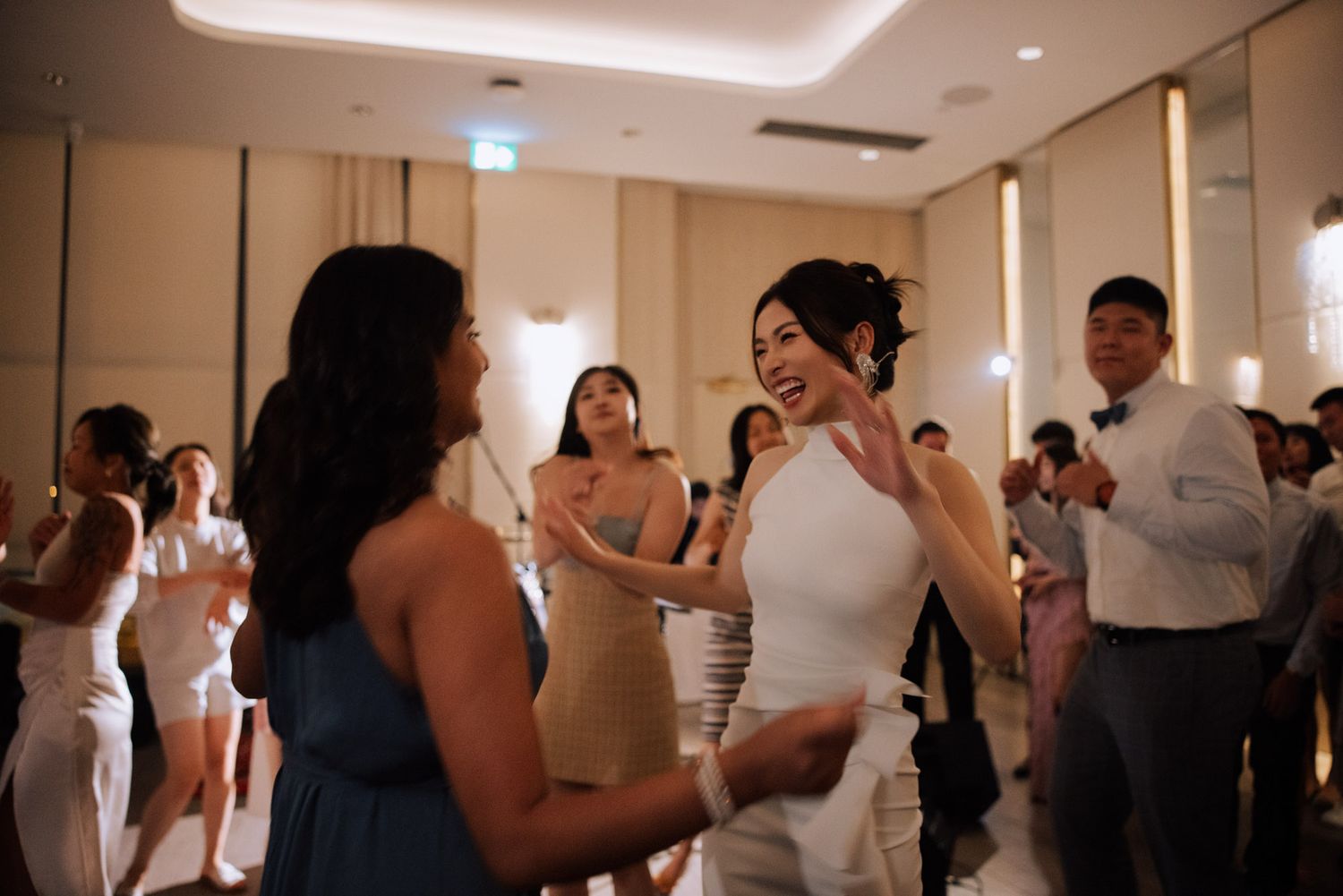 Bride in white dress dancing joyfully with guests at elegant wedding reception in a ballroom.