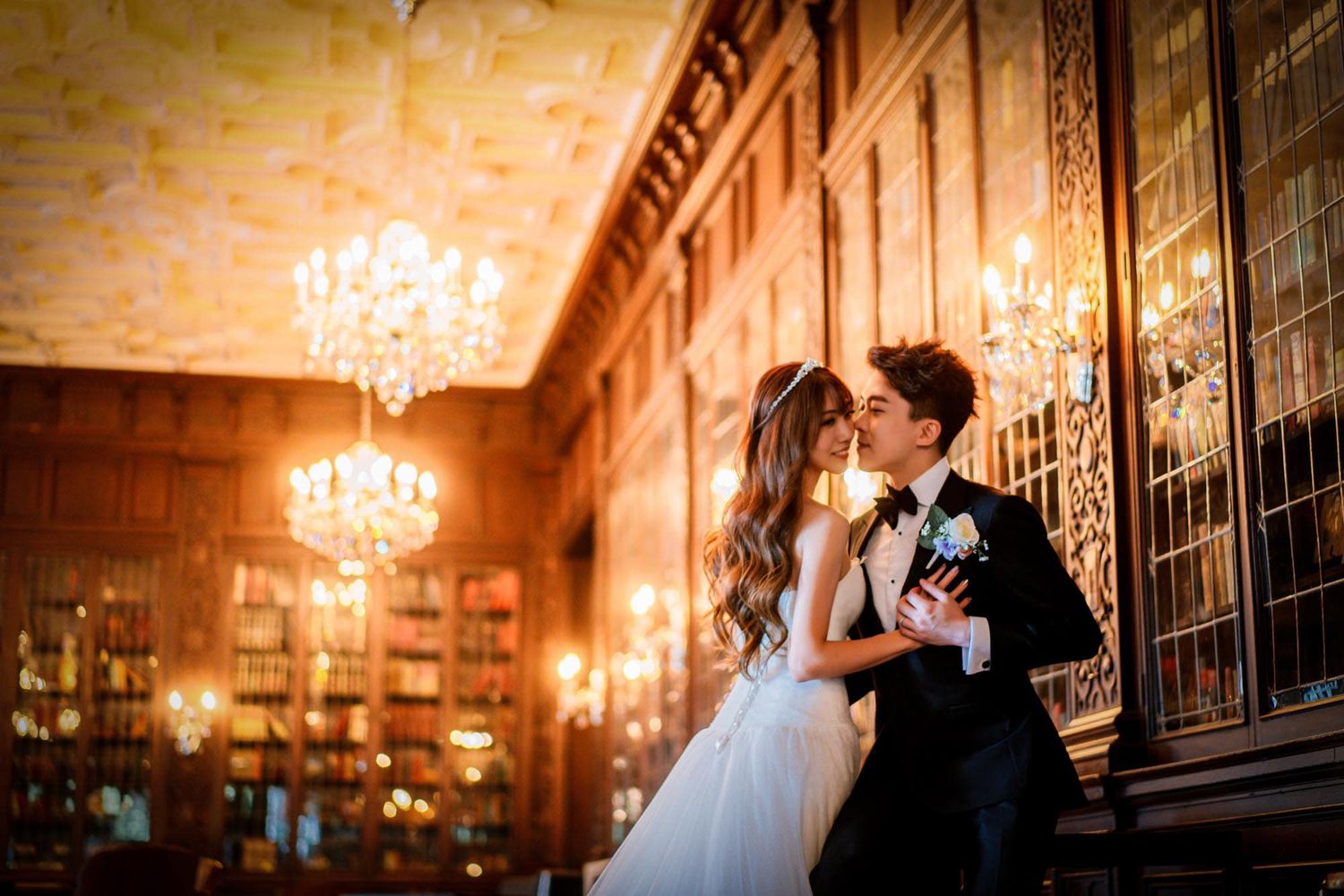 Bride and groom share a tender kiss in an ornate chandelier-lit library during their wedding.
