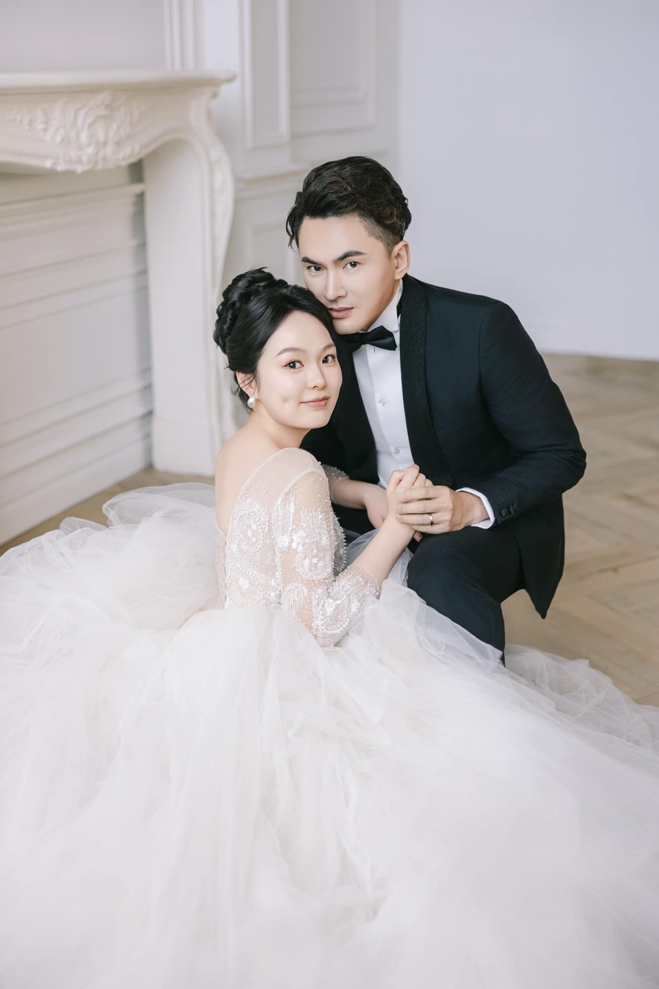 Elegant couple in wedding attire sitting together in a bright white room.