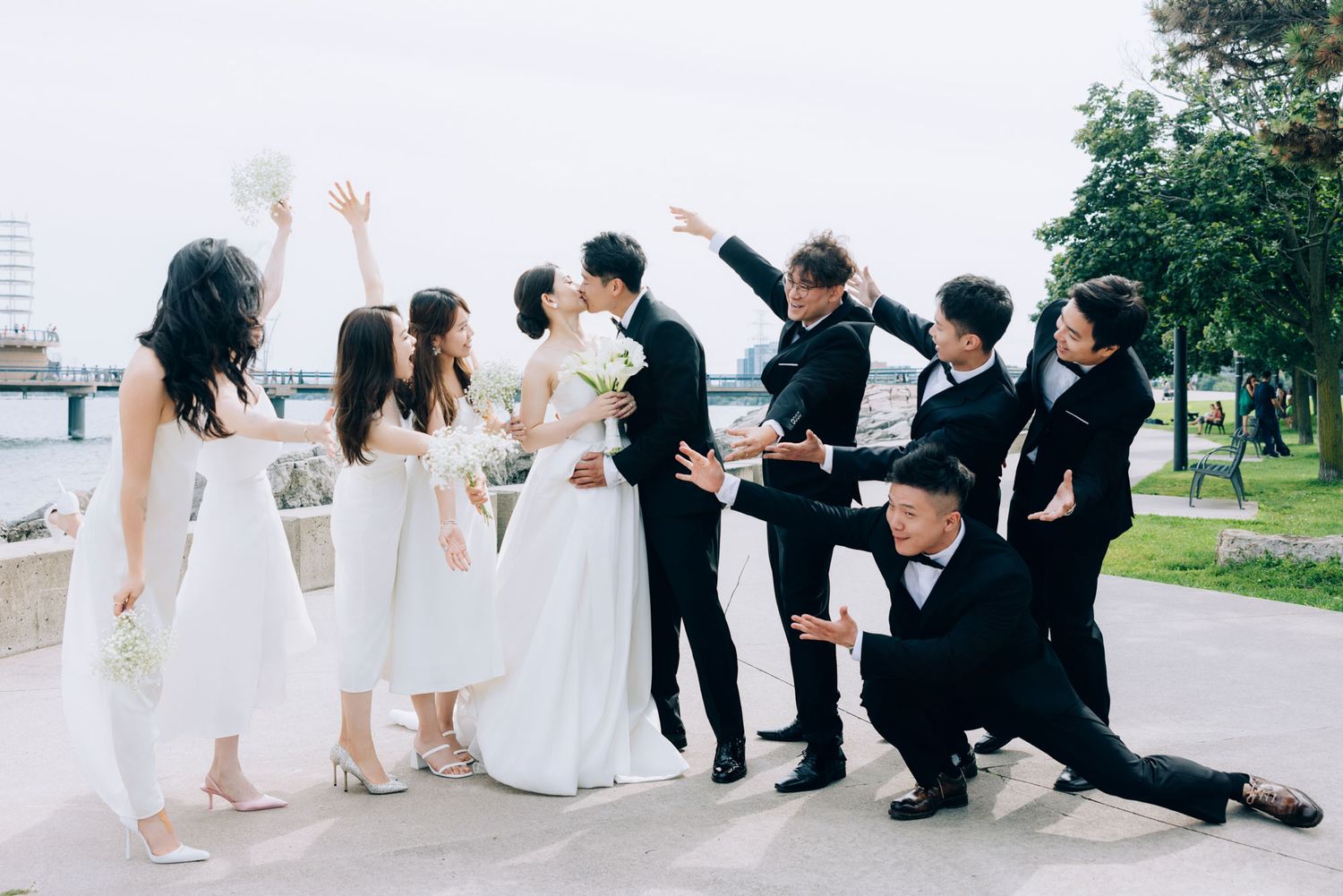 Wedding party celebrates as bride and groom kiss surrounded by cheering attendants.