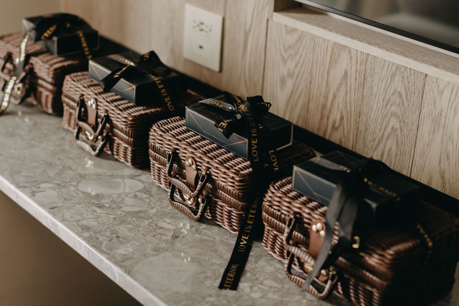 Row of wicker gift boxes tied with black ribbons on marble counter as wedding favors.
