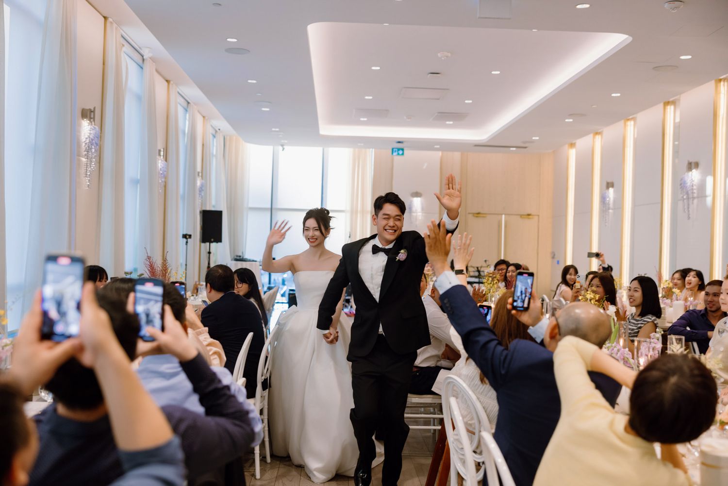 Bride and groom waving to cheering guests during their grand wedding reception entrance.
