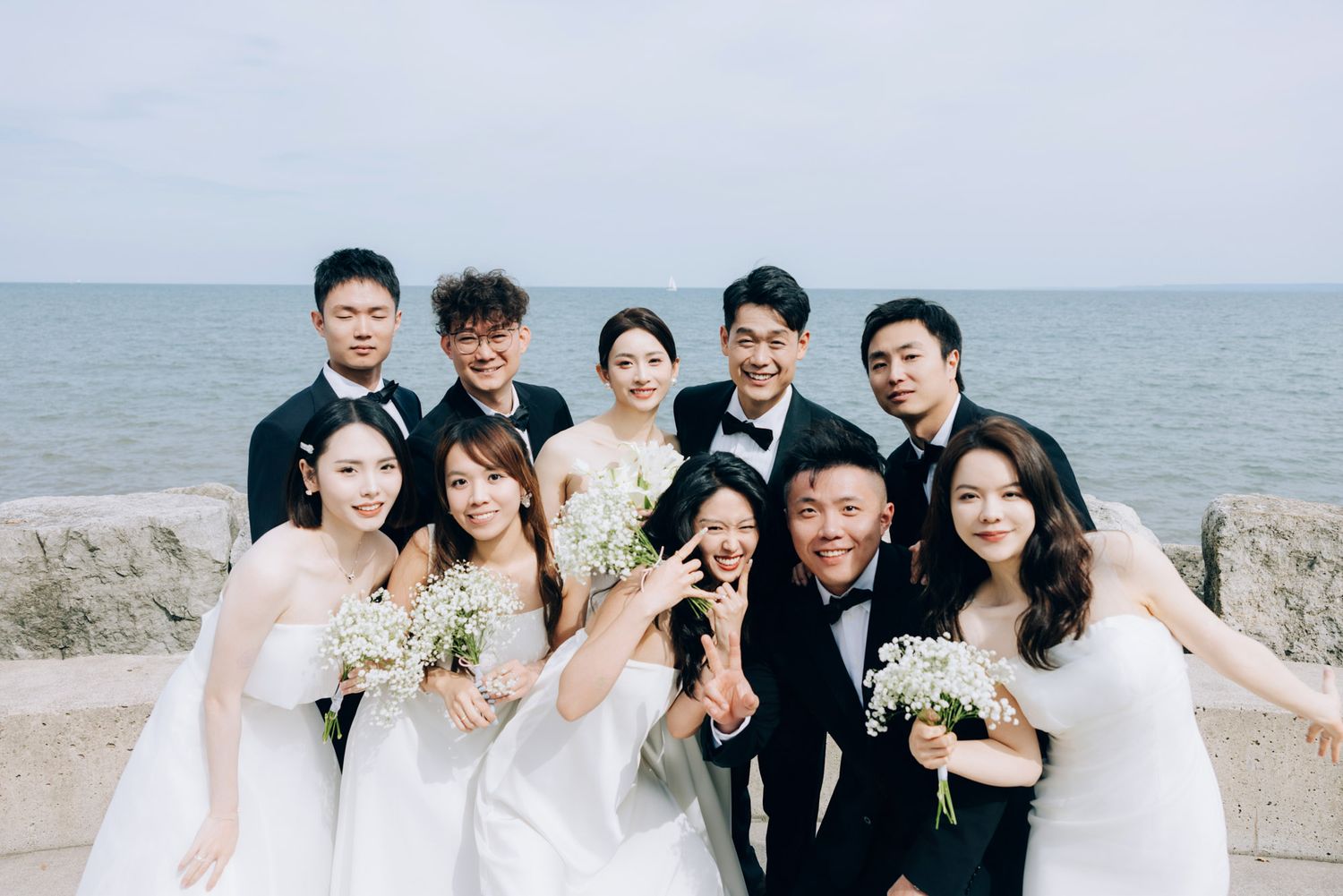 Joyful wedding party group photo with bride, groom, and friends celebrating by the sea.