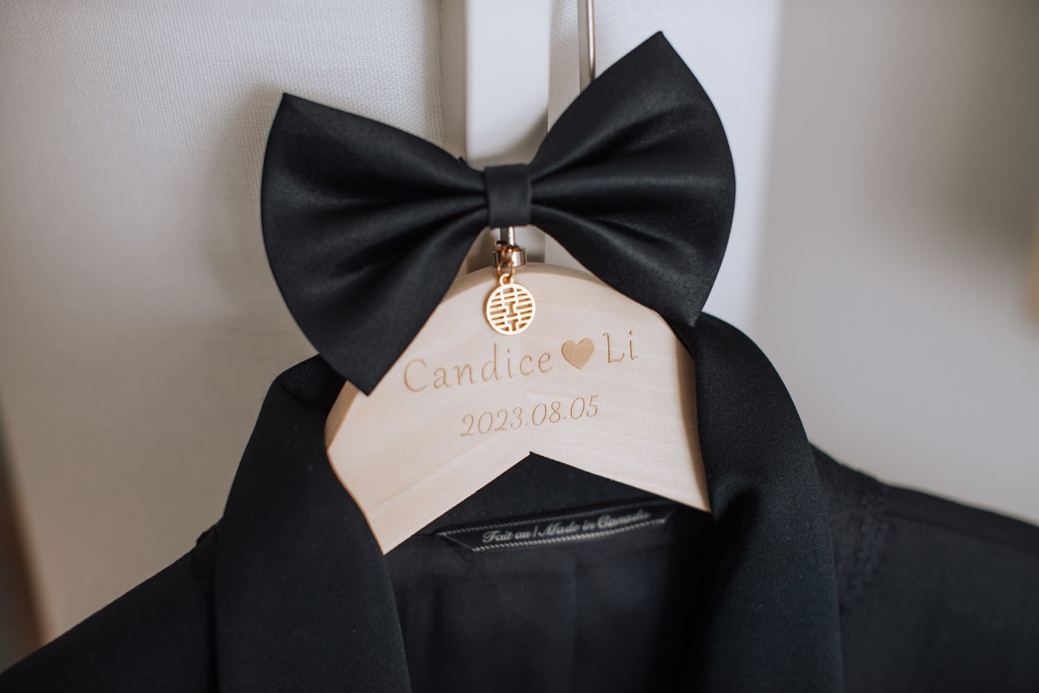 Personalized wooden wedding hanger with black bow tie and gold charm engraved with couple names.