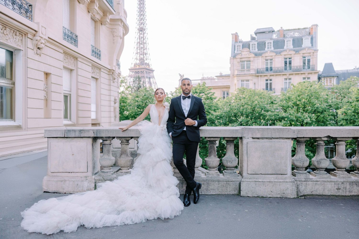 Bride and groom pose elegantly on a Parisian balcony with the Eiffel Tower in the background.
