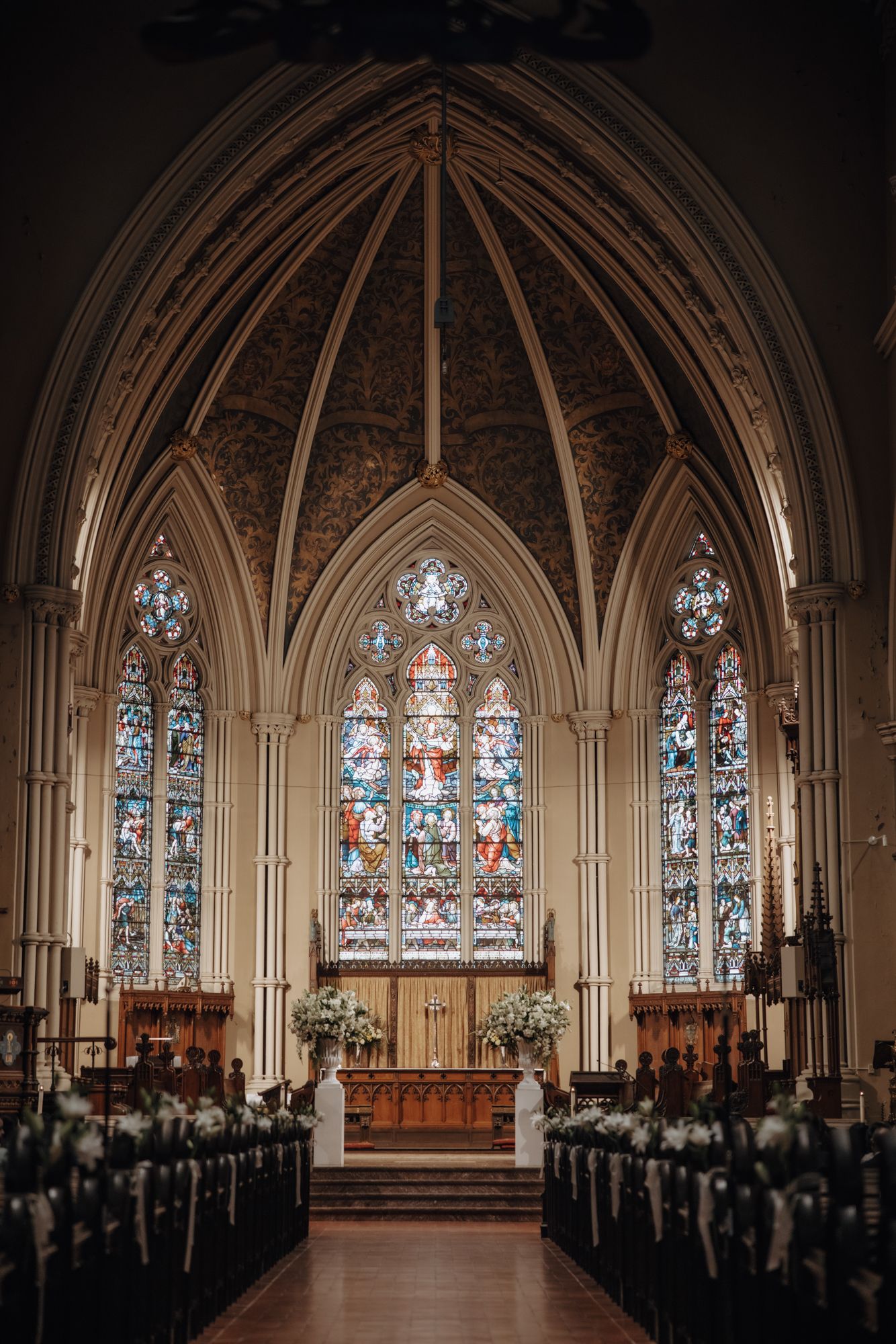 Gothic church interior with a vaulted ceiling, stained glass windows and pews decorated with white floral arrangements for a wedding.