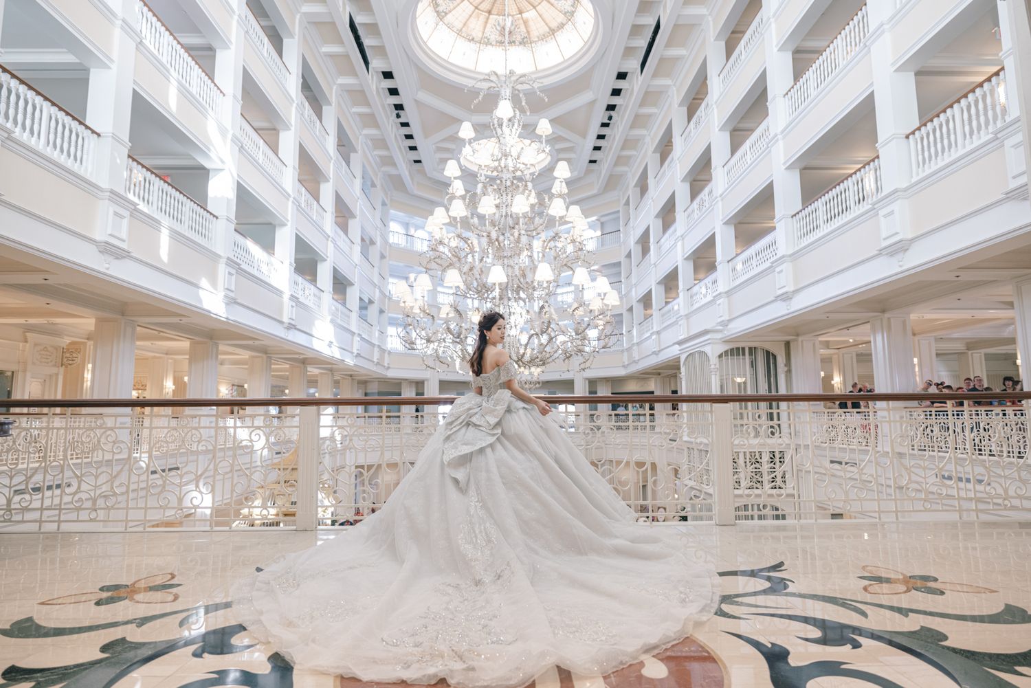 Bride twirls in stunning white ball gown under grand crystal chandelier in luxurious hotel atrium.