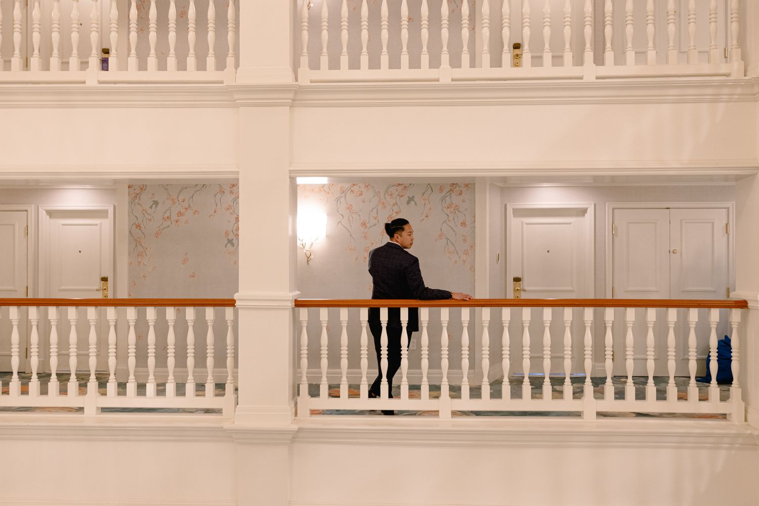 Person standing on a white balcony railing inside an elegant hotel atrium with classical architecture.