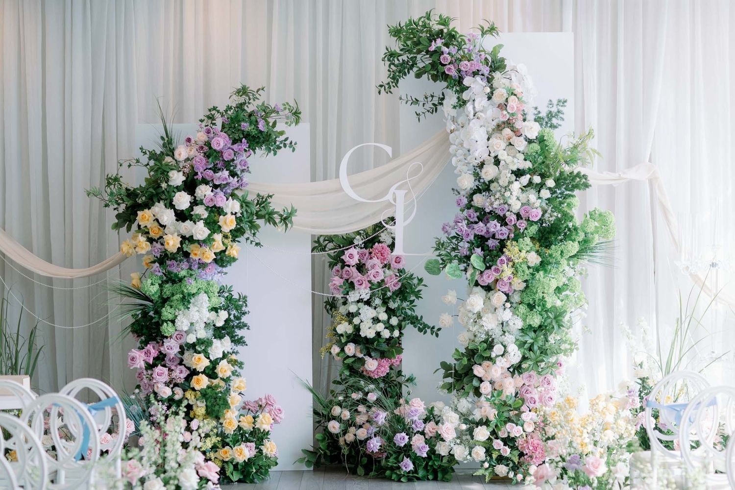 Stunning wedding ceremony backdrop featuring two tall floral columns with colorful pastel roses and greenery.