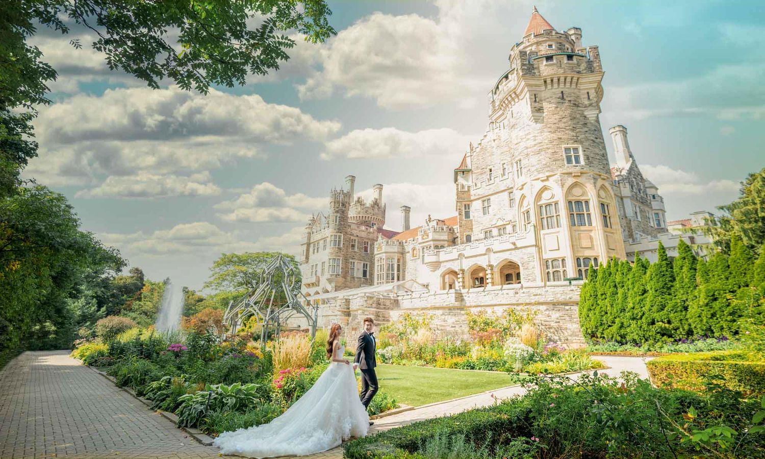 Bride and groom pose in front of a grand castle surrounded by lush gardens on their wedding day.