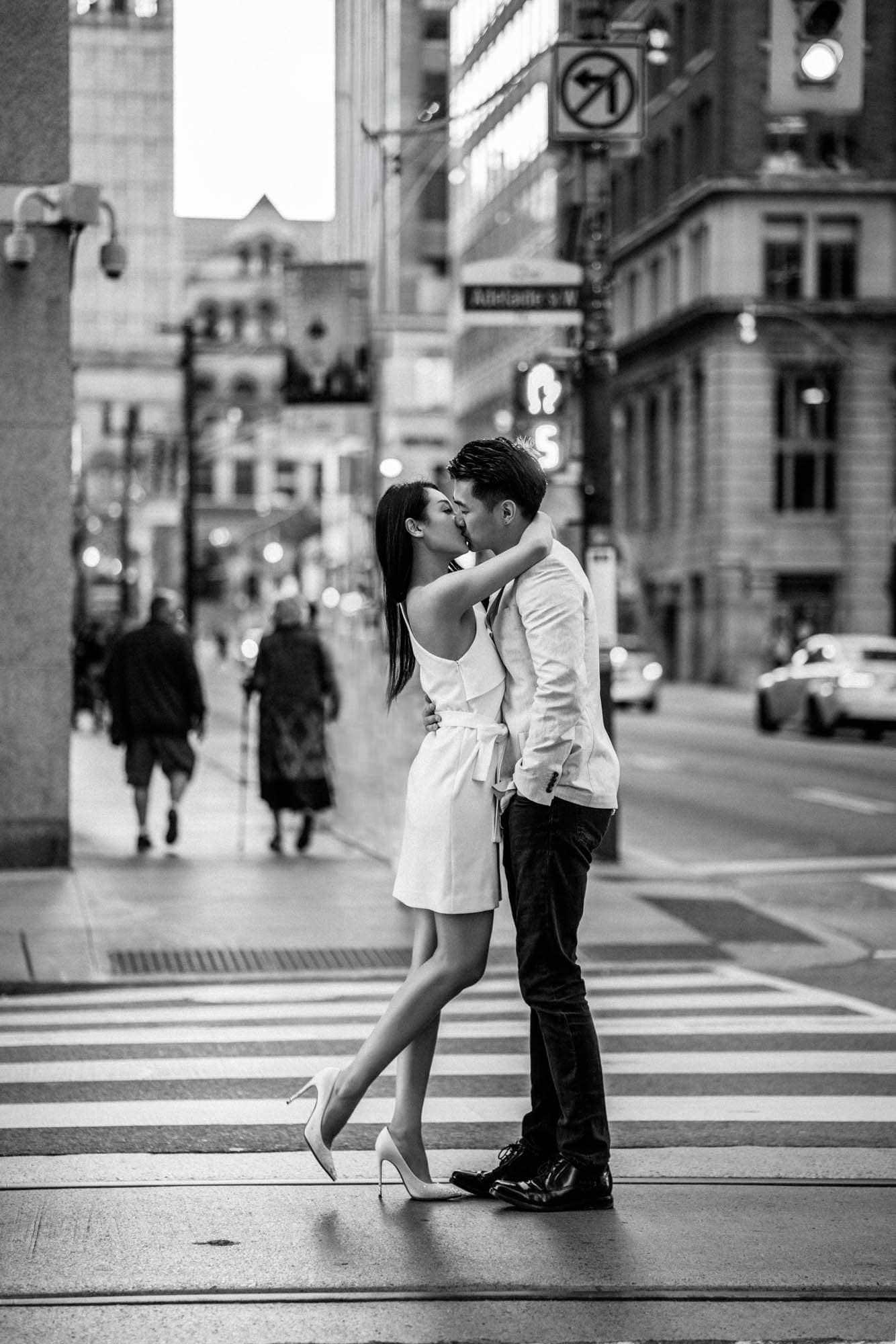 Black and white photo of couple kissing on a city crosswalk.