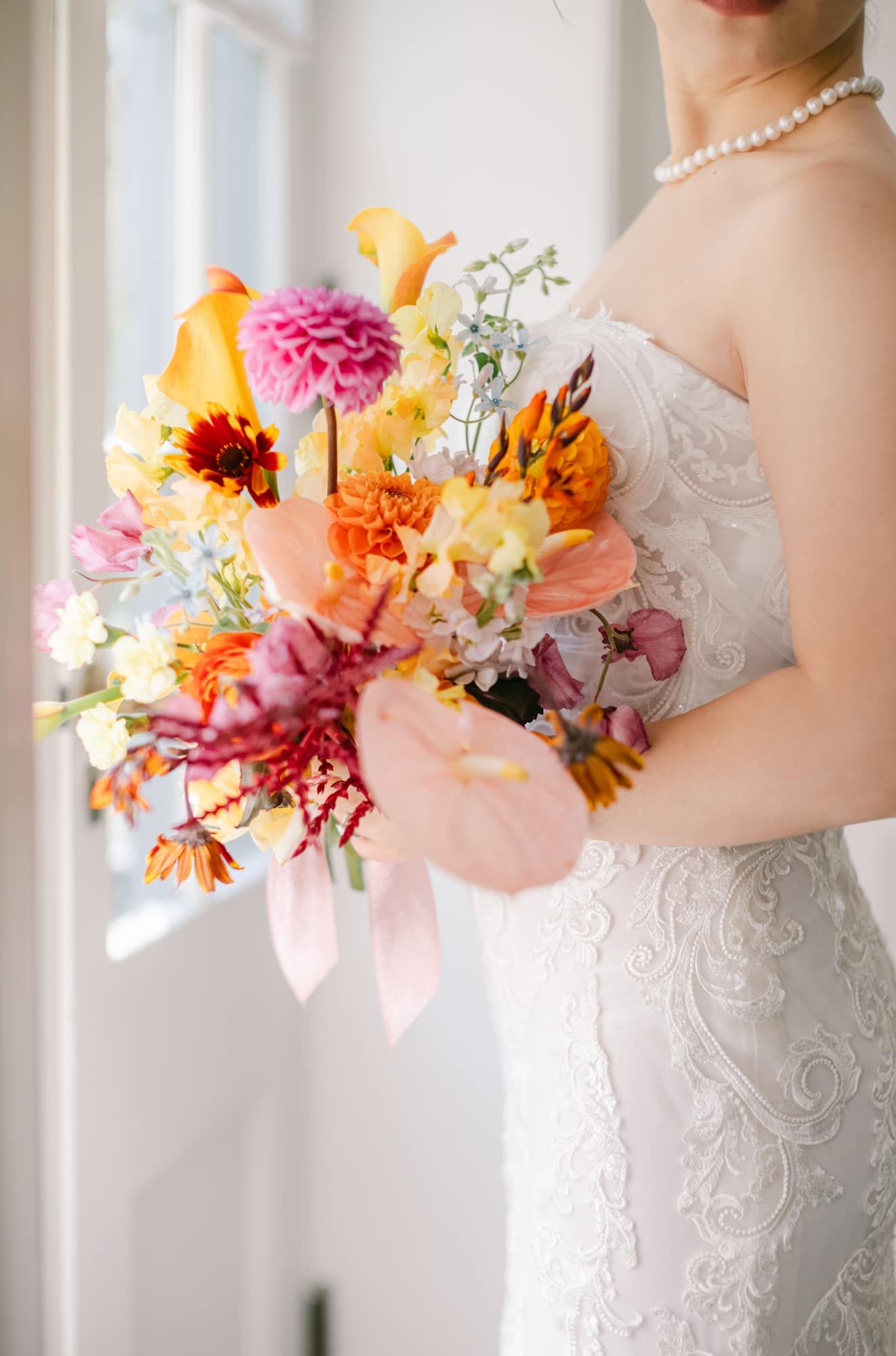 Bride holding a vibrant orange and pink bouquet wearing a lace wedding gown.