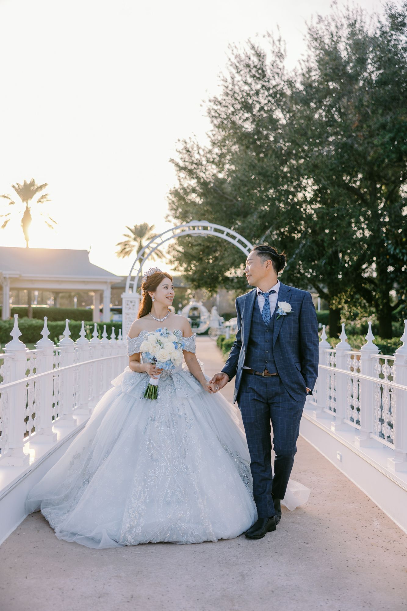Bride and groom hold hands on white bridge at sunset at Disney World resort.