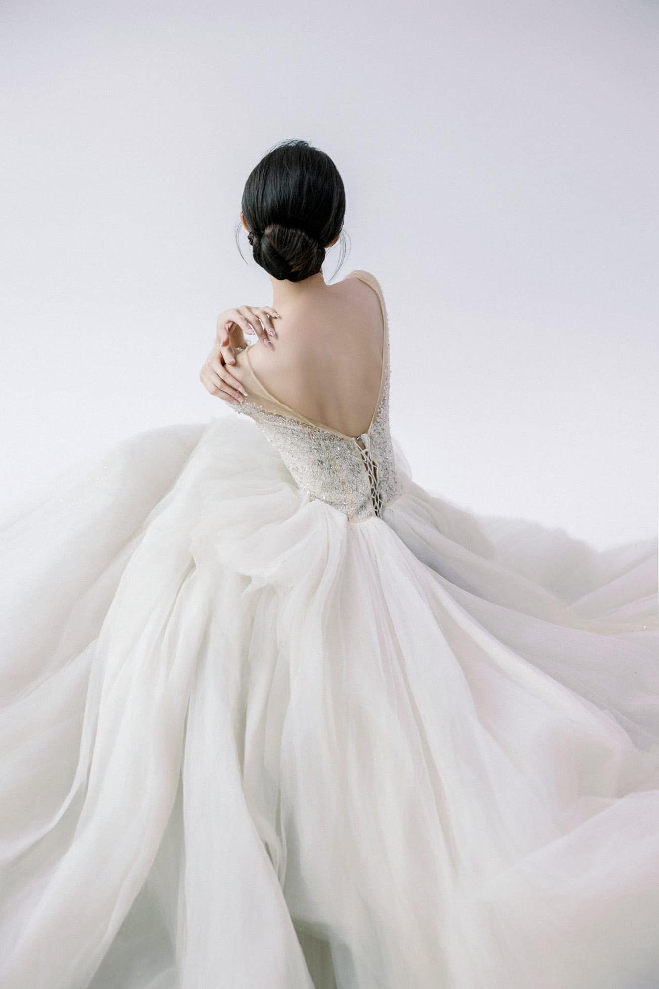 Bride in elegant white backless wedding gown with flowing skirt and long sleeves, showcasing intricate beaded bodice details.