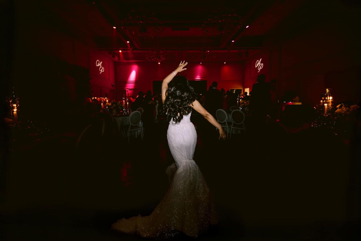 Bride in white mermaid gown dancing elegantly under dramatic red lighting at wedding reception.