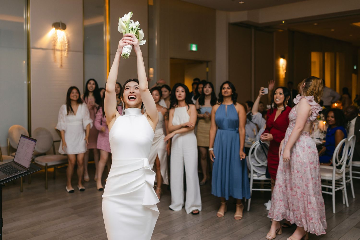Bride joyfully throws her white bouquet into the air during the bouquet toss at wedding reception.