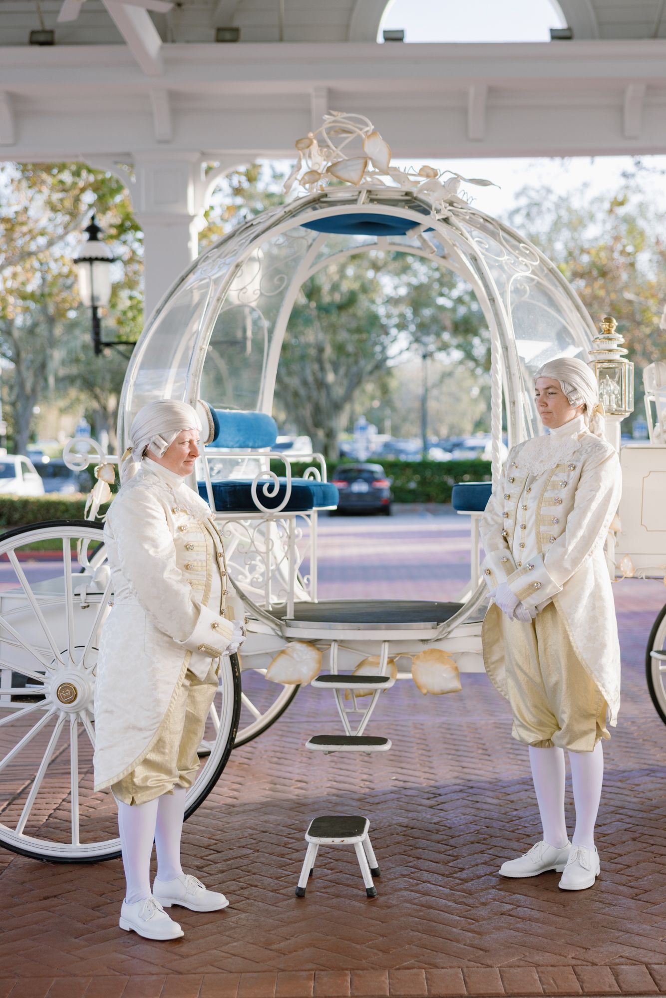 Two footmen in period costumes stand beside Cinderella glass carriage at Disney World resort.